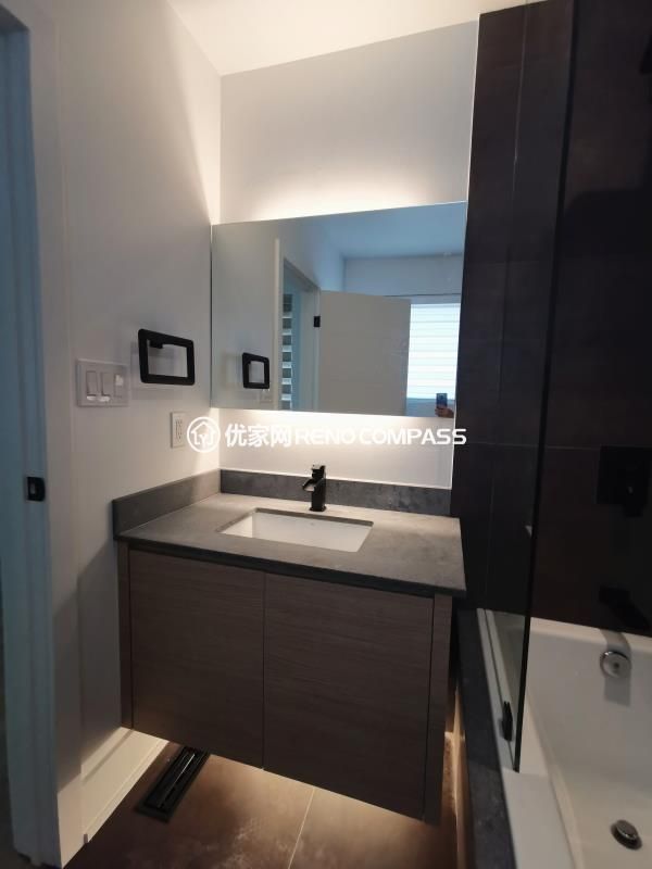 Compact bathroom vanity completed as part of a North York interior renovation. This space features a custom wood vanity with an integrated sink, stone countertop, and a wall-mounted mirror with concealed LED lighting. The clean layout maximizes functionality within a narrow footprint while maintaining a modern, uncluttered appearance. Neutral finishes and precise detailing reflect a bathroom renovation designed and built by a Toronto renovation company focused on efficient use of space and long-term durability.