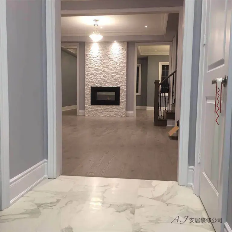 This Scarborough interior renovation highlights a welcoming entrance view leading into a modern living space. The design features marble-look floor tiles at the entry, warm wood flooring throughout the main area, and a textured stone fireplace feature wall as the focal point. Recessed lighting, neutral grey walls, and elegant trim details create a clean and contemporary interior layout, enhancing both visual depth and everyday functionality for this Scarborough home.