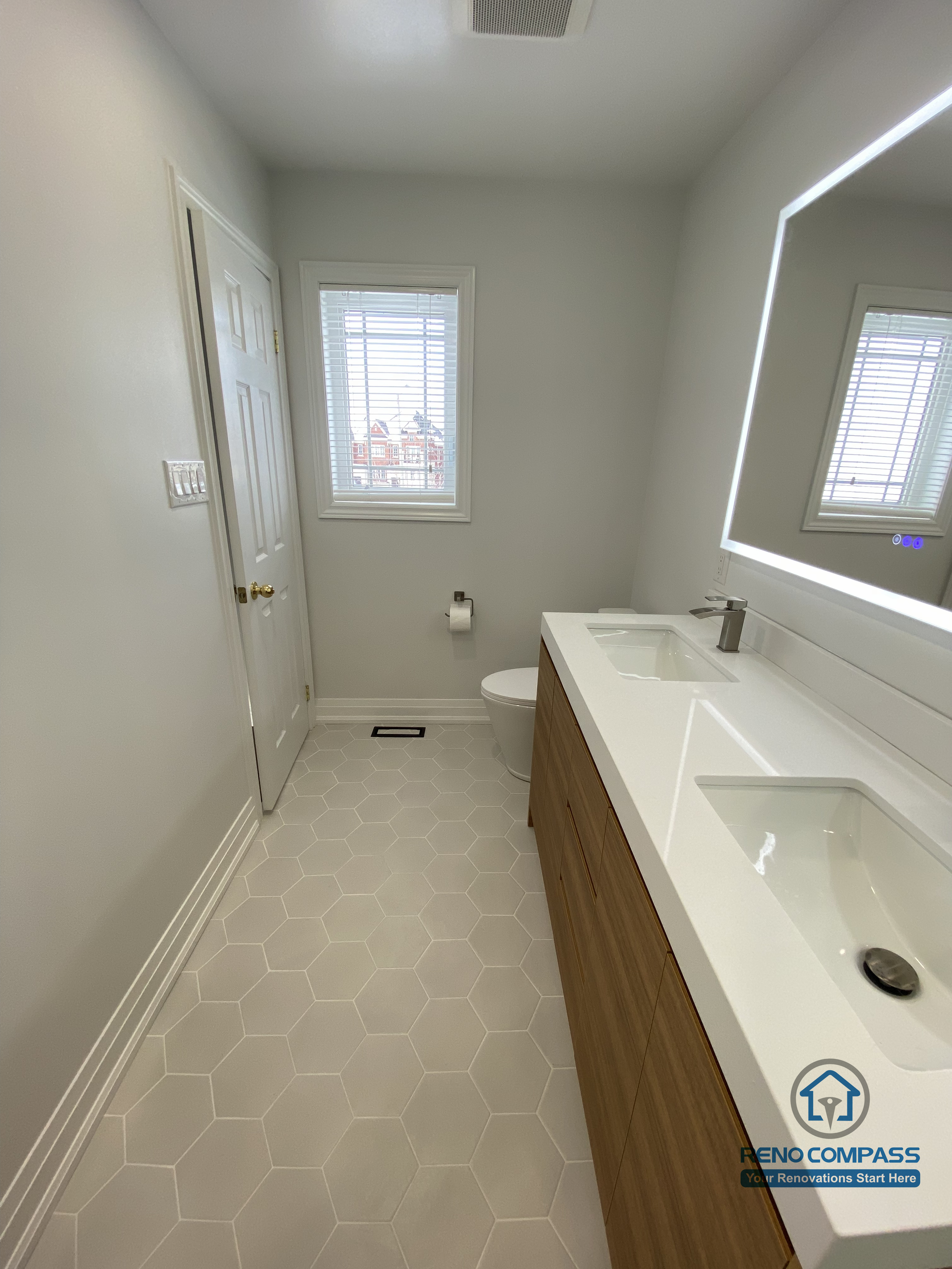 This Markham bathroom renovation highlights a clean, functional layout featuring a custom vanity paired with an LED backlit mirror for even, glare-free lighting. The long countertop provides generous daily-use space while maintaining a streamlined appearance. Hexagon floor tiles add subtle texture and slip resistance, enhancing safety and durability in a high-moisture environment. Neutral wall tones and natural light from the window create a bright, calm atmosphere that supports everyday comfort. Completed by a Toronto renovation company, Reno Compass Inc., this bathroom renovation reflects careful space planning, material coordination, and long-term usability for modern Markham homes.