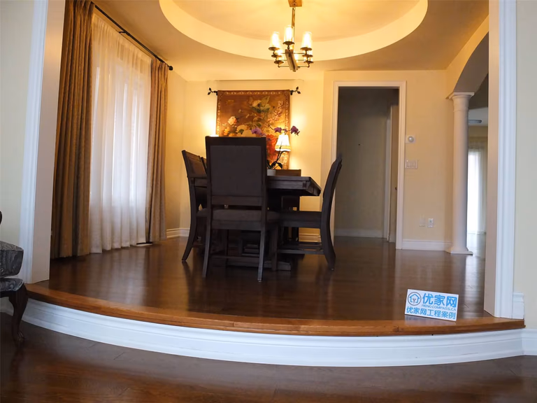 This Aurora flooring renovation highlights a beautifully upgraded dining room featuring rich hardwood flooring and elegant interior details. The polished wood floor complements the elevated dining area, curved step design, and warm ceiling lighting, creating a sophisticated and inviting atmosphere. Completed by a professional Toronto renovation company, the flooring installation enhances both the visual appeal and durability of this refined dining space.