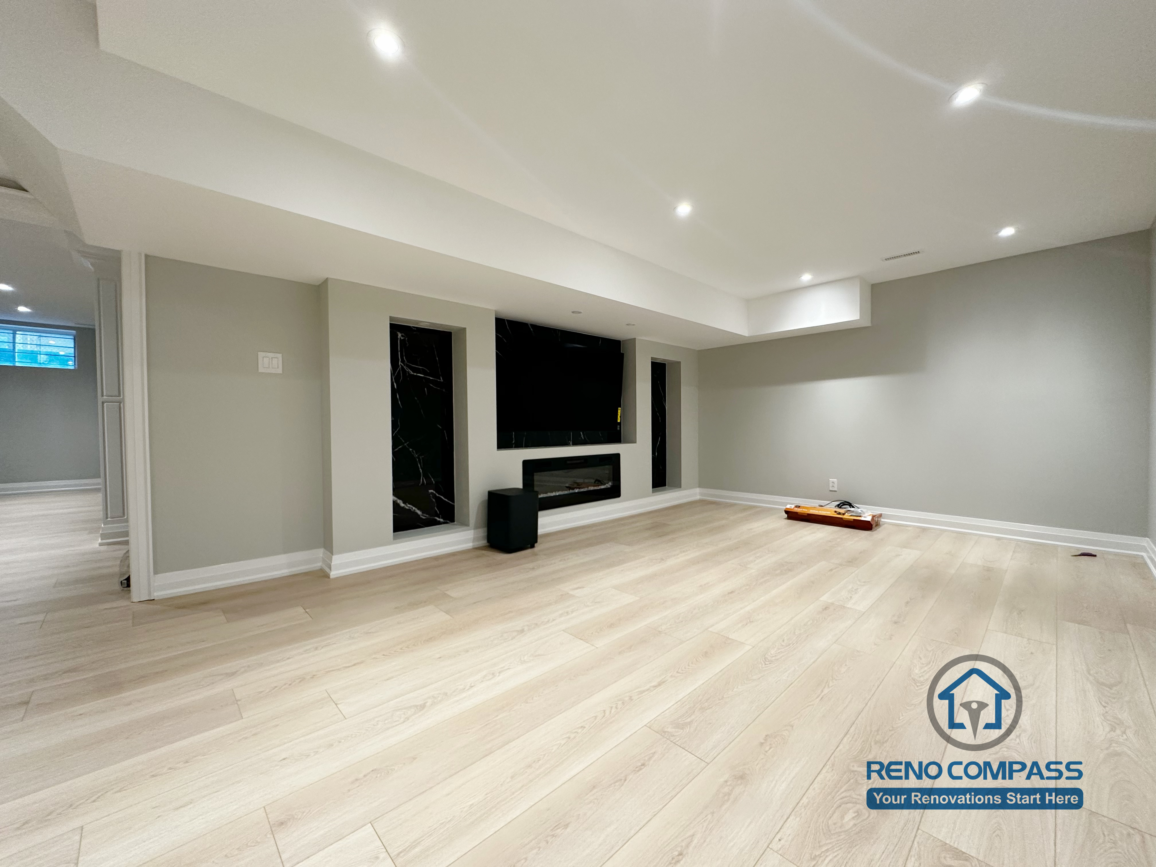 Finished basement renovation in Richmond Hill showcasing a modern feature wall with built-in fireplace, TV niche, black marble-style panels, and recessed lighting for a sleek entertainment space.