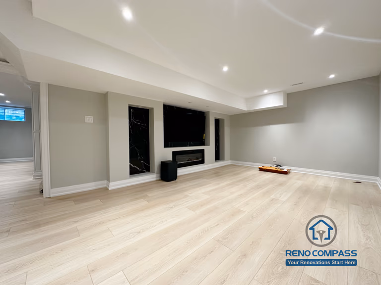 Finished basement renovation in Richmond Hill showcasing a modern feature wall with built-in fireplace, TV niche, black marble-style panels, and recessed lighting for a sleek entertainment space.