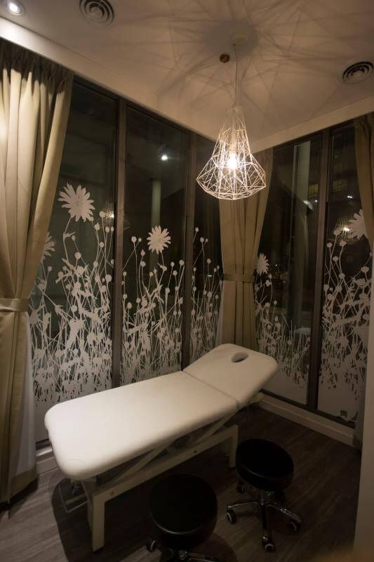 Private treatment room completed as part of a Toronto spa commercial renovation. The space features a professional massage bed, decorative frosted glass panels with floral patterns, warm lighting, and soft curtains, creating a relaxing and comfortable environment for spa treatments and wellness services.
