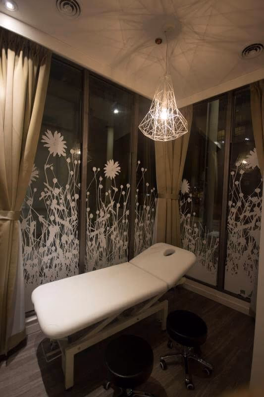 Private treatment room completed as part of a Toronto spa commercial renovation. The space features a professional massage bed, decorative frosted glass panels with floral patterns, warm lighting, and soft curtains, creating a relaxing and comfortable environment for spa treatments and wellness services.