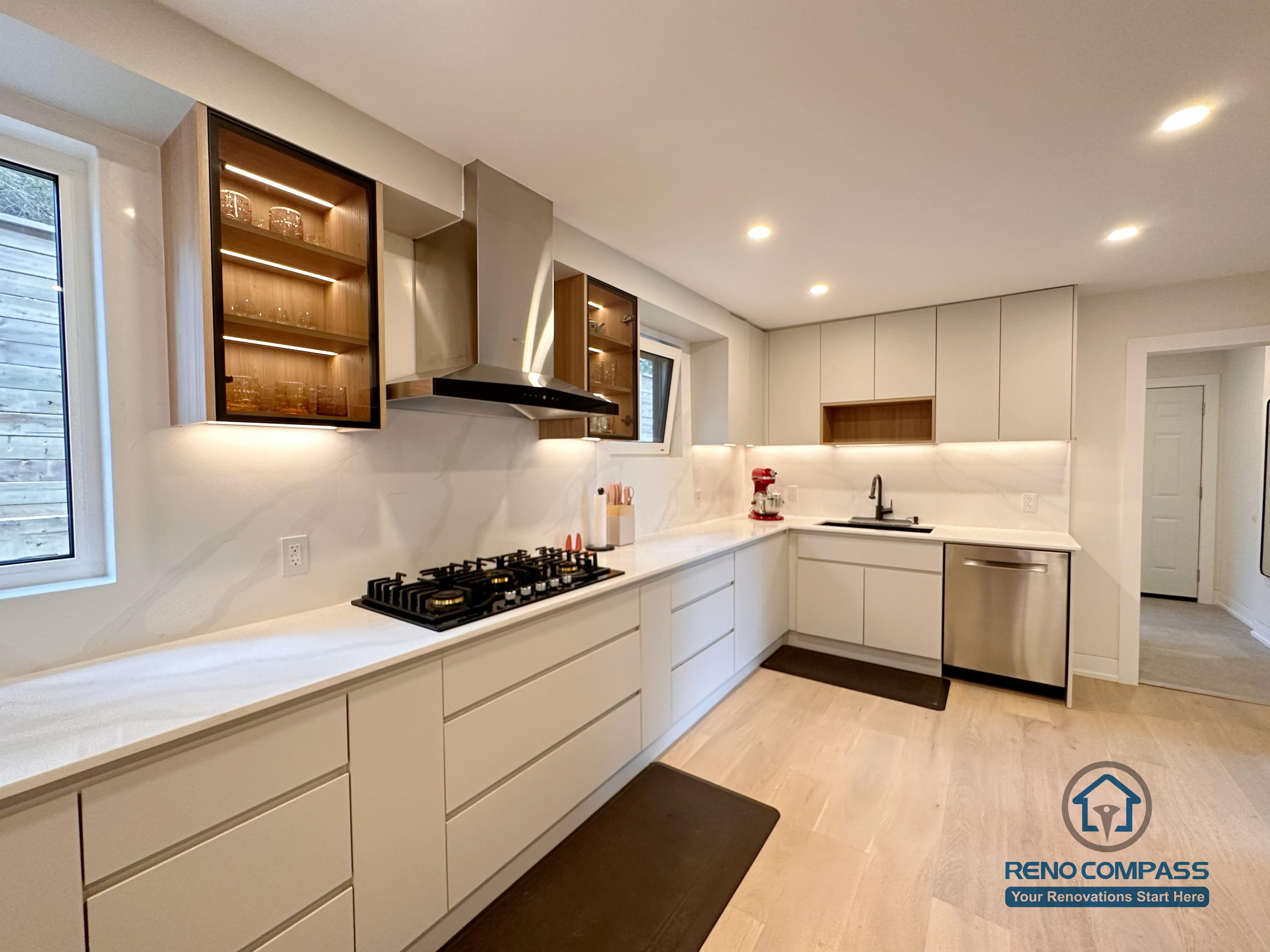 A modern L-shaped kitchen renovation in Toronto featuring custom cabinetry, extended countertop workspace, integrated appliances, and glass display cabinets with LED lighting. This thoughtfully designed kitchen layout improves workflow efficiency while maintaining a clean, contemporary aesthetic, completed by a professional Toronto renovation company.