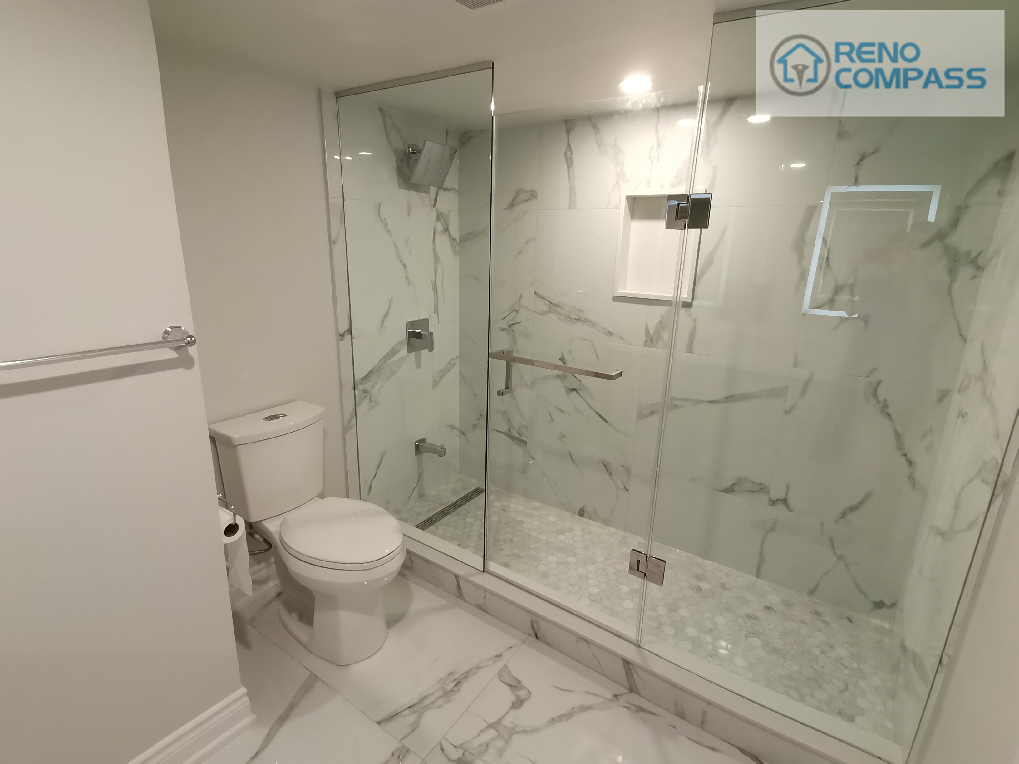 This Woodbridge basement bathroom features a frameless glass walk-in shower finished with large-format marble-style wall tiles and a slip-resistant mosaic shower base. A built-in wall niche adds practical storage while maintaining a clean, uninterrupted surface. The compact layout integrates the toilet seamlessly beside the shower, maximizing space efficiency without sacrificing comfort. Neutral finishes and clear glass help keep the basement bathroom bright, open, and suitable for daily use or guest accommodation.