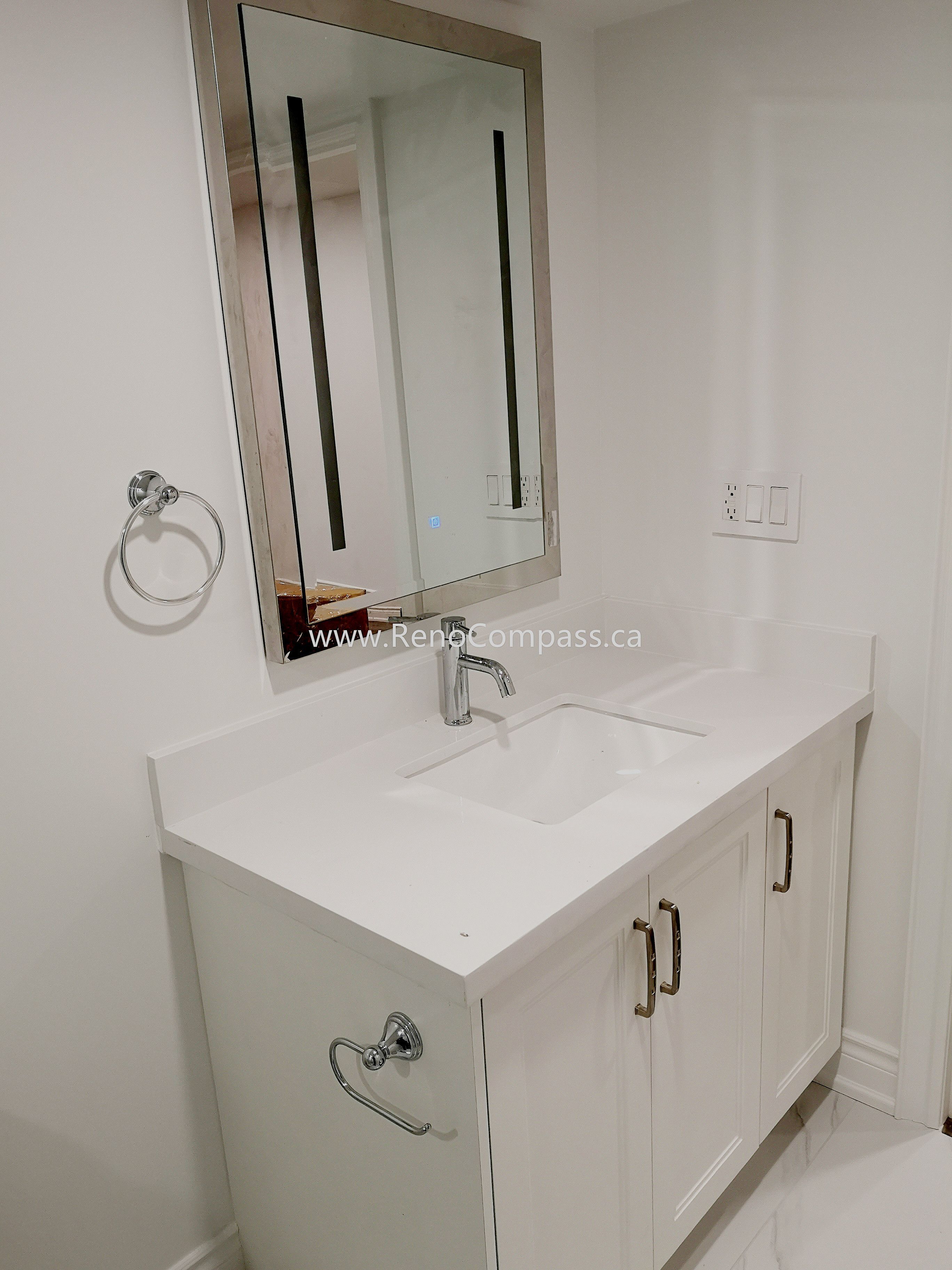 This Vaughan basement renovation features a modern bathroom vanity installation with a sleek white quartz countertop, under-mount sink, and contemporary chrome faucet. The clean white cabinetry provides both storage and a minimalist aesthetic, perfectly matching the bright and modern basement design. Completed by Reno Compass Inc., this basement bathroom upgrade enhances functionality while maintaining a stylish and cohesive interior renovation finish.