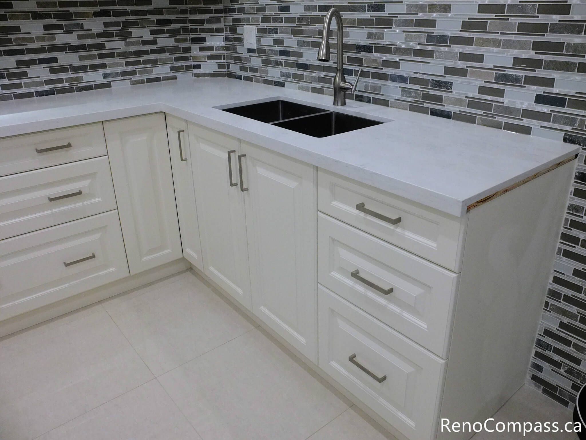 This Markham basement kitchen detail highlights a clean quartz countertop paired with an undermount sink and modern faucet. The white shaker cabinets and mosaic tile backsplash create a cohesive and contemporary look, while the practical layout ensures durability and ease of maintenance for everyday use. Completed by a trusted Toronto Renovation Company, Reno Compass Inc.
