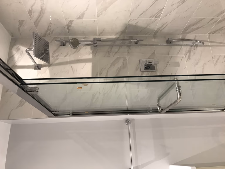 High-end Toronto bathroom renovation showcasing a frameless glass shower enclosure, rainfall shower system, and marble-style porcelain wall tiles that create a sleek and contemporary design.