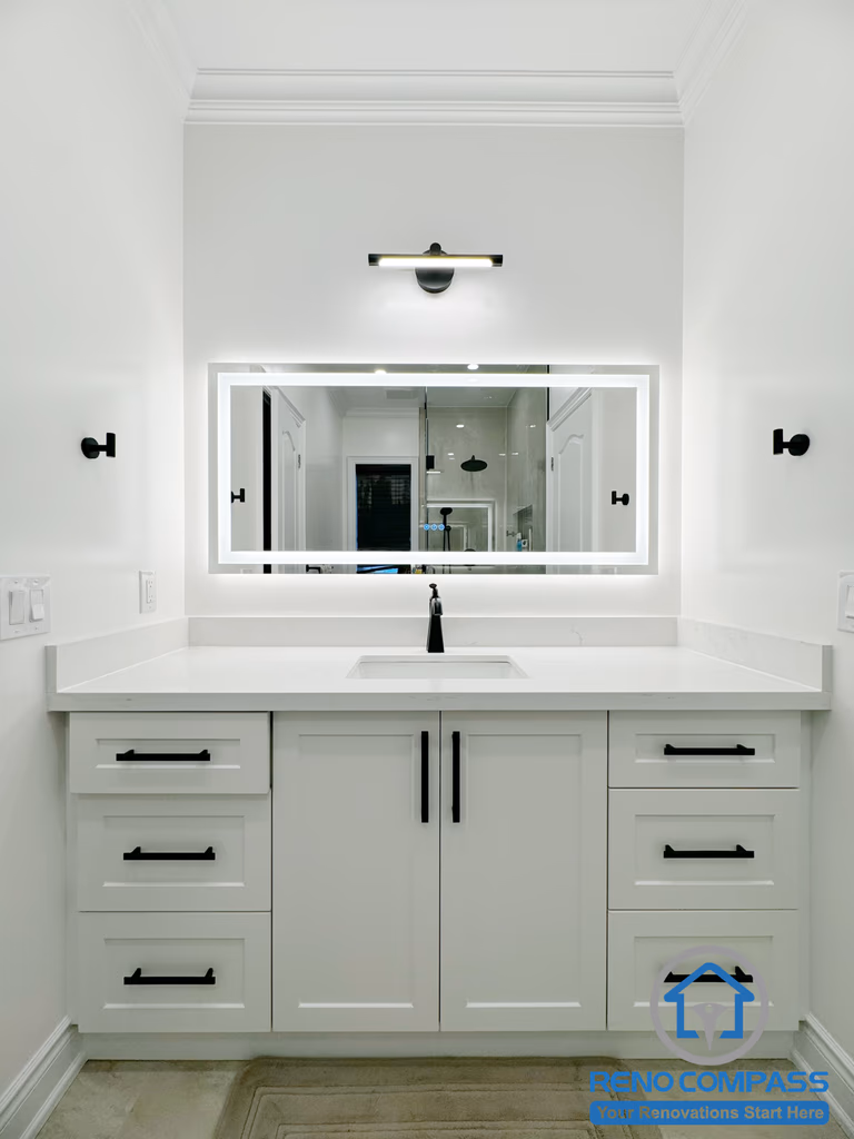 This Vaughan bathroom renovation features a custom double vanity with a quartz countertop, integrated storage drawers, and matte black hardware. A backlit LED mirror and modern wall-mounted lighting provide balanced illumination while enhancing the clean, minimalist design. Completed by a professional Toronto Renovation Company, this vanity area combines practical storage, modern finishes, and refined craftsmanship for a bright and functional bathroom space.