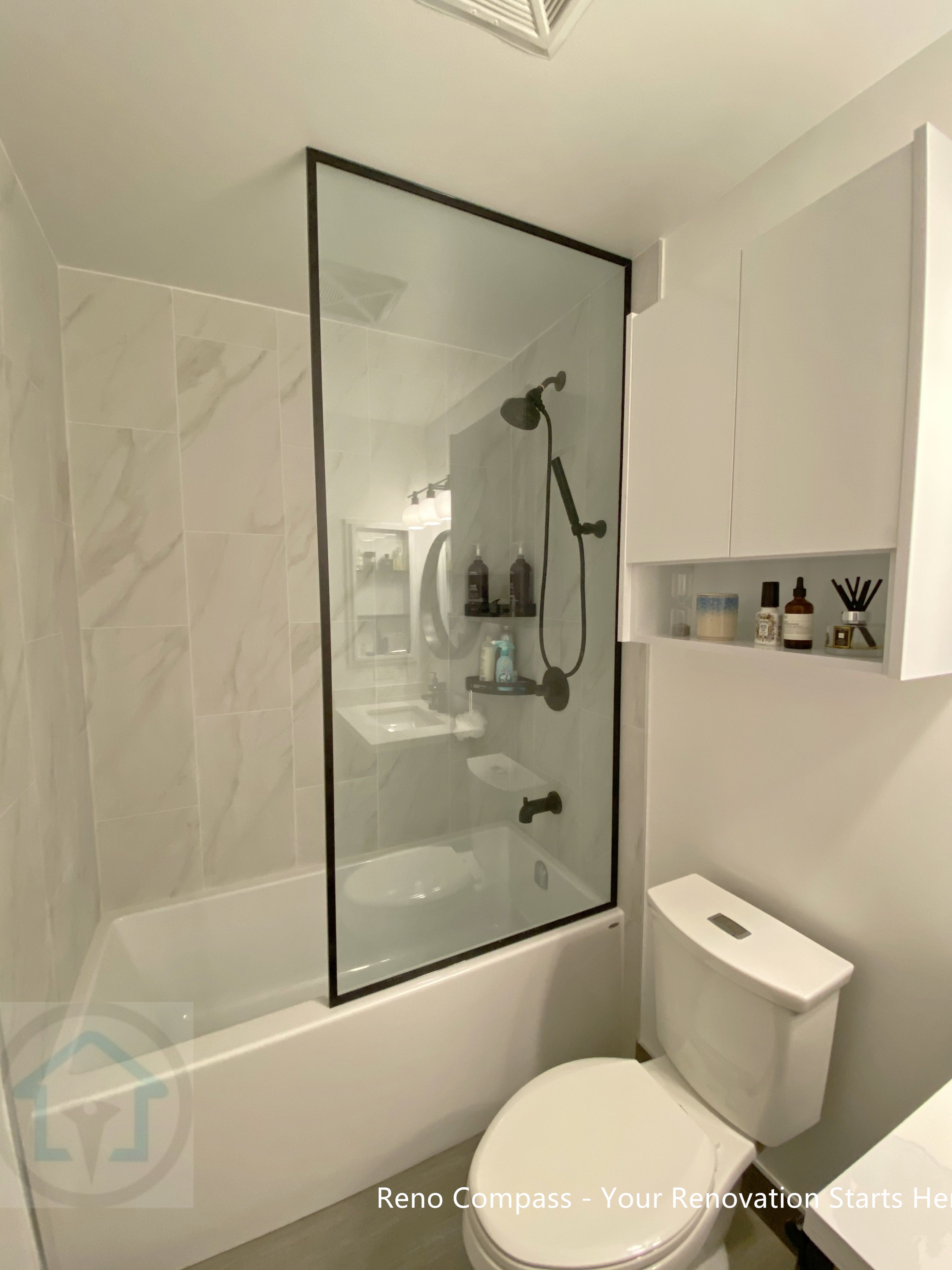 This North York condo bathroom renovation features a clean tub and shower combination with a custom black-framed glass panel, marble-look wall tiles, and matte black fixtures. Built-in wall storage improves daily usability while maintaining a streamlined, modern aesthetic ideal for compact condo bathrooms.