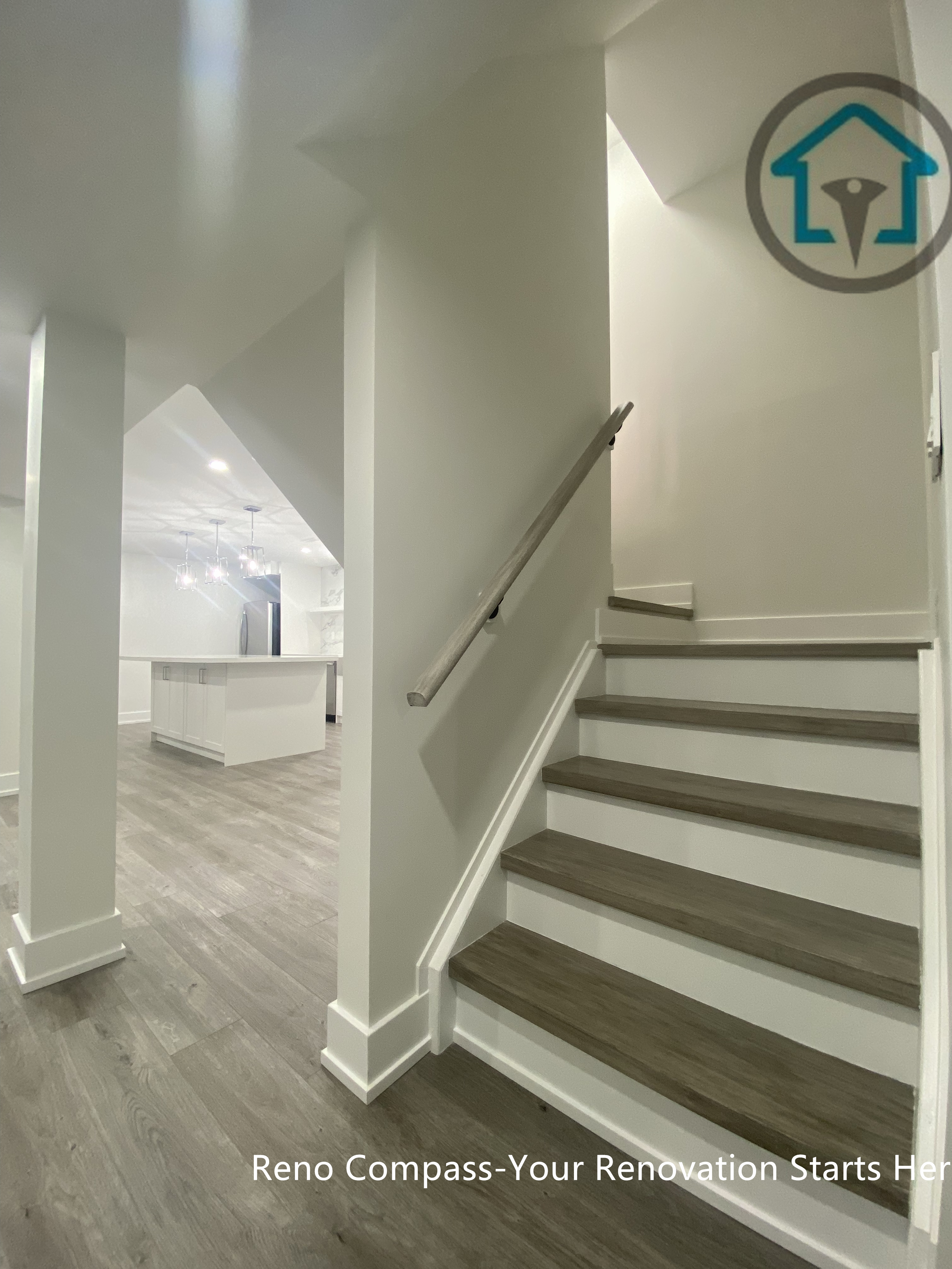 This image highlights the staircase and circulation area of a Newmarket basement renovation completed by a professional Toronto renovation company. The basement features modern wood-look flooring, clean white walls, and a newly finished staircase with matching treads and minimalist handrails. The open layout connects seamlessly to the basement kitchen area, enhancing flow, brightness, and overall usability while maintaining a clean and contemporary design style ideal for rental or family living.