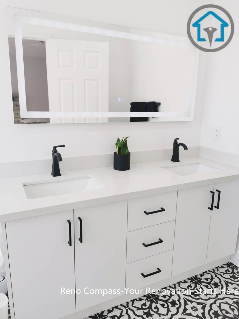 This Ajax bathroom renovation showcases a clean and functional double vanity design with a seamless white countertop and integrated sinks. Matte black faucets and cabinet hardware add strong contrast to the bright cabinetry, while the patterned floor tiles introduce visual interest without overwhelming the space. The layout is designed for daily comfort, combining practical storage with a modern, timeless aesthetic.