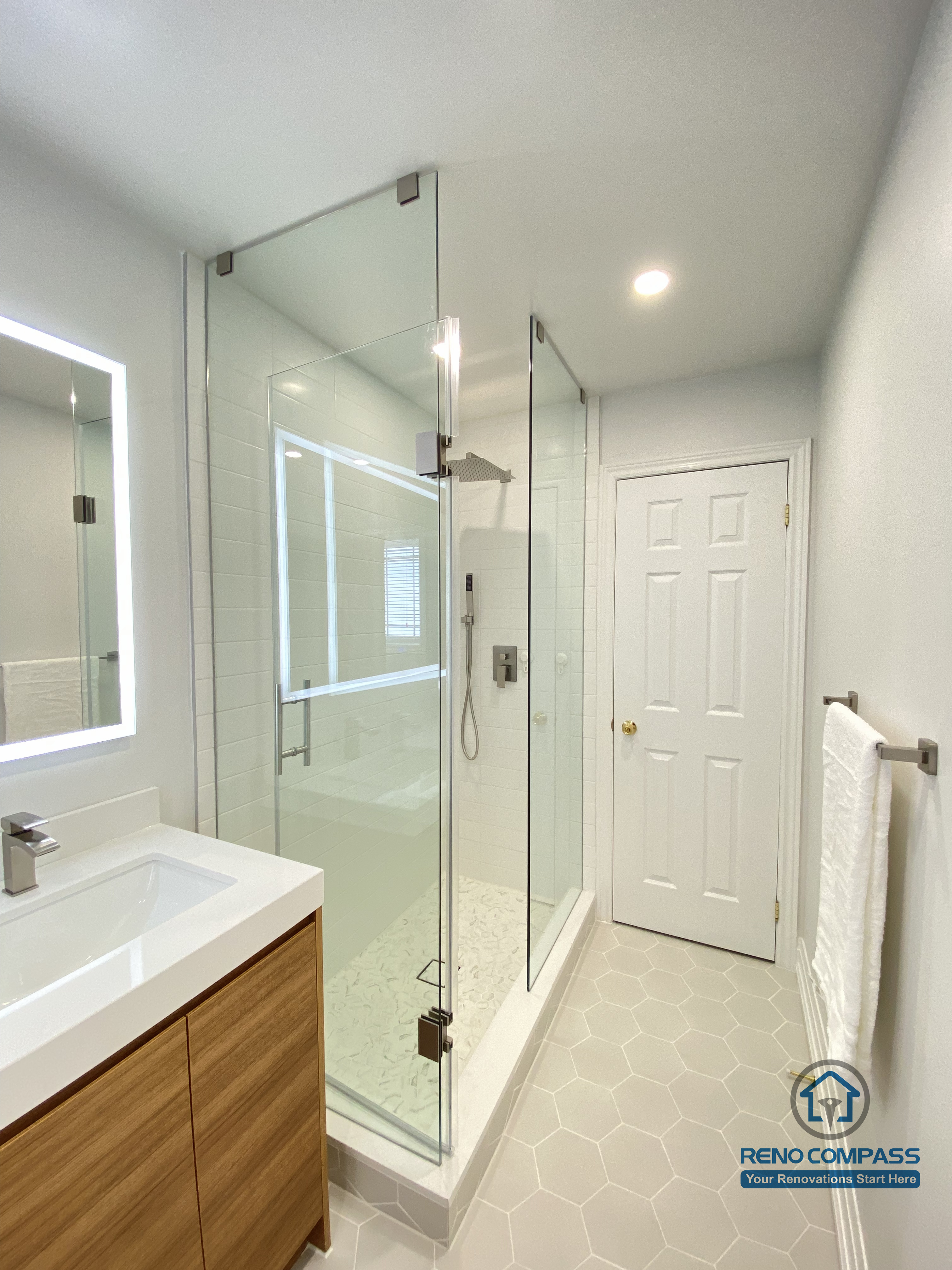This Markham bathroom renovation features a modern walk-in shower designed with clear glass panels to enhance openness and natural light flow. The layout improves daily circulation while maintaining privacy and ease of use. A custom vanity with integrated storage provides a clean, organized appearance, paired with a sleek countertop and illuminated mirror for improved visibility. Slip-resistant hexagon tile flooring enhances safety and durability in a high-moisture environment. Completed by a Toronto renovation company, Reno Compass Inc., this bathroom renovation reflects a practical and refined approach to material selection, proportion control, and long-term usability for Markham homes.