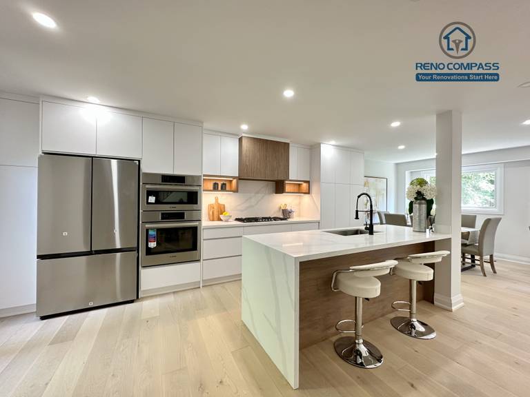 This Richmond Hill interior renovation features a bright open-concept kitchen and living space with custom white cabinetry, integrated stainless steel appliances, a waterfall kitchen island, and wide-plank hardwood flooring. Designed and completed by a Toronto renovation company, the layout enhances natural light, functionality, and modern living comfort for contemporary family homes.
