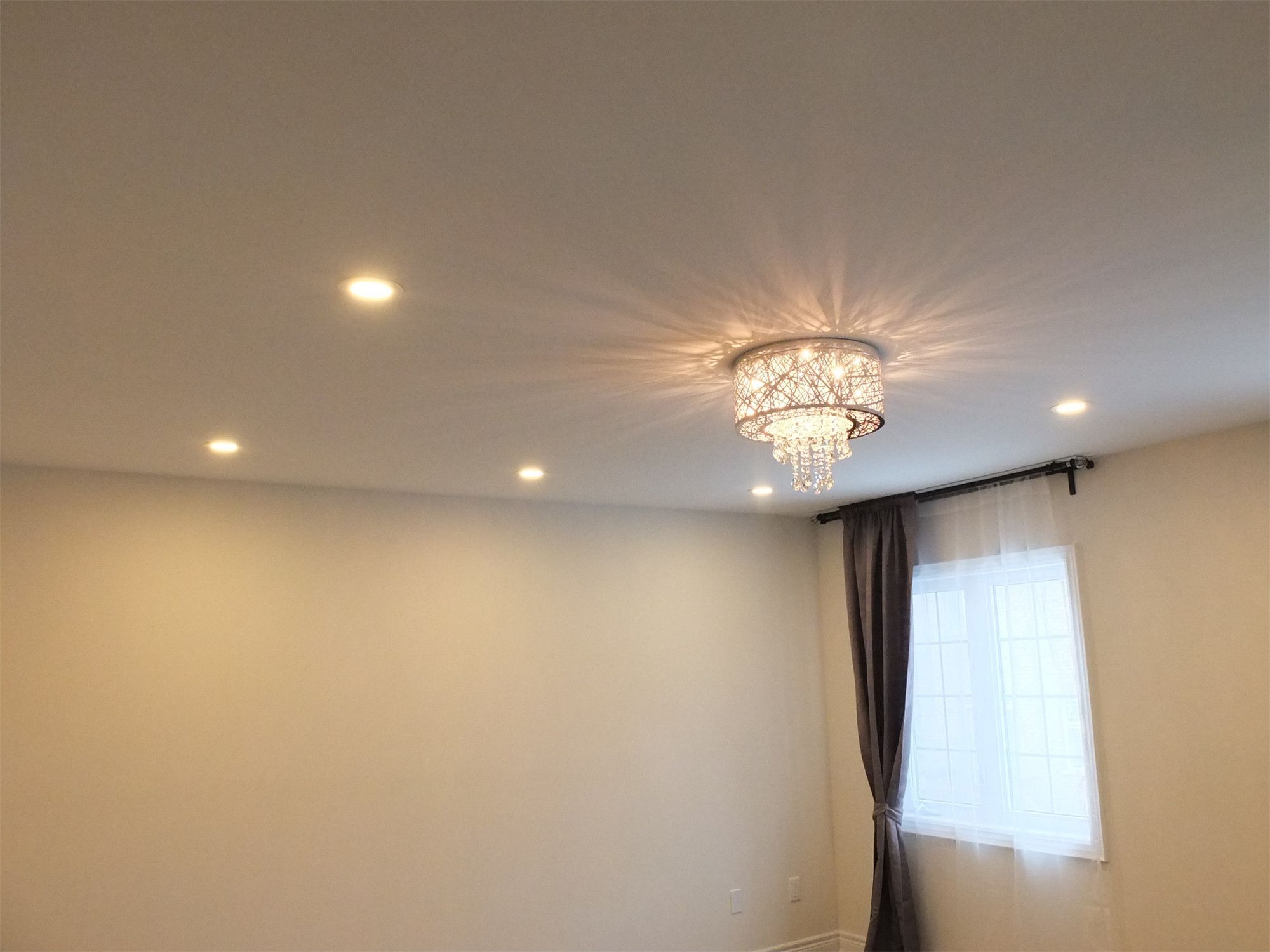 This Kleinburg interior renovation highlights a refined bedroom lighting design featuring recessed pot lights combined with an elegant crystal ceiling fixture. The chandelier adds a touch of luxury while the pot lights provide balanced ambient lighting throughout the room. Paired with soft neutral wall finishes and natural light from the window, the space feels bright, calm, and comfortably modern.