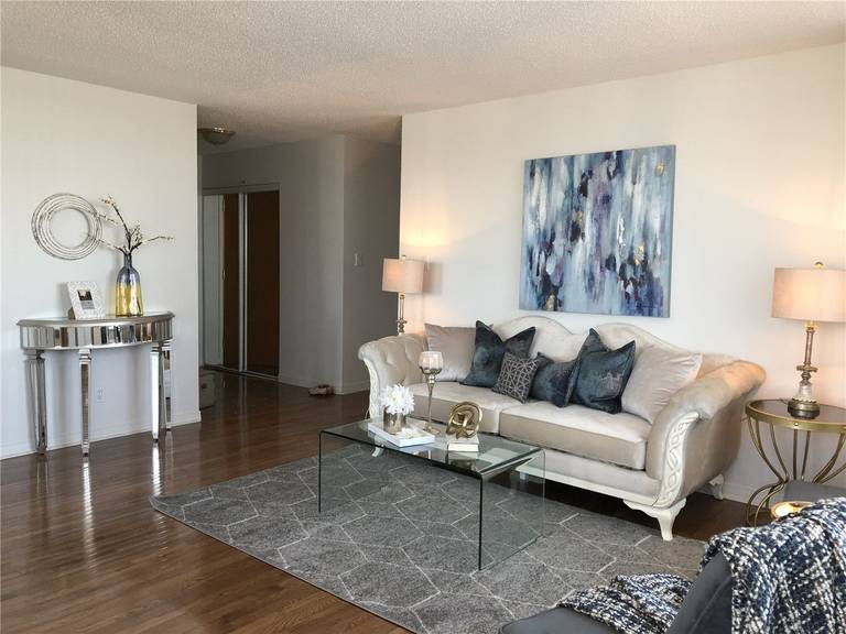 This Toronto interior design pre-sale staging features a bright and modern living room with polished hardwood flooring, a neutral-tone sofa, glass coffee table, and contemporary artwork. Thoughtful furniture placement and coordinated décor create a spacious, elegant atmosphere that enhances natural light and flow. Completed by a professional 多伦多装修公司, this staged living space helps elevate property value and allows potential buyers to envision a comfortable and stylish home environment.