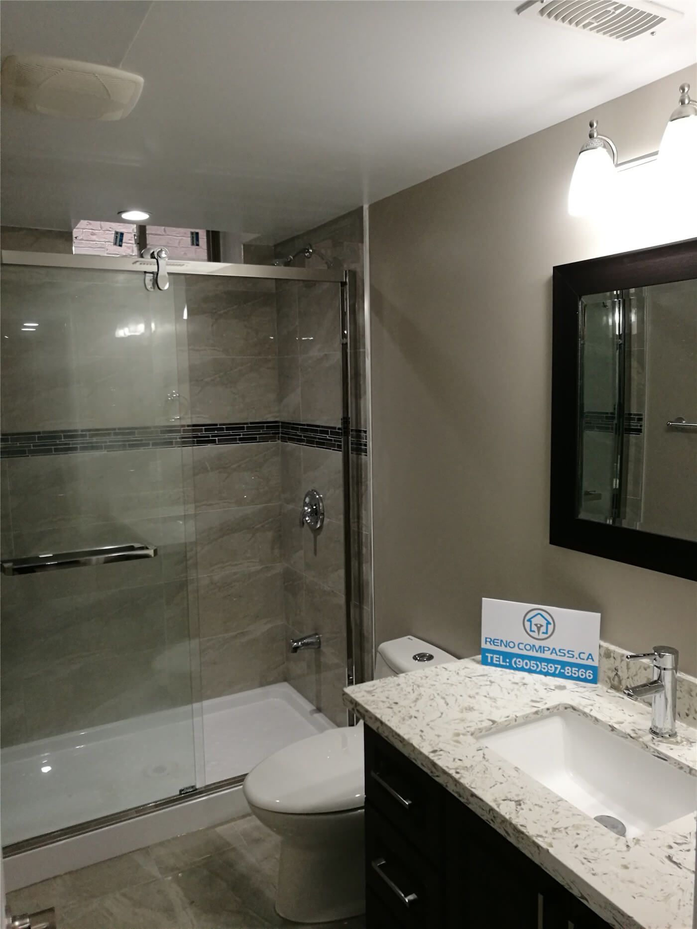 This image shows a completed basement bathroom from a Newmarket interior renovation project. The bathroom features a frameless glass shower enclosure, large-format wall tiles with decorative accent detailing, and a modern vanity with a stone countertop. Integrated lighting and neutral finishes create a clean, bright, and functional space. Completed by a professional Toronto renovation company, this bathroom renovation improves comfort, water efficiency, and overall interior value.