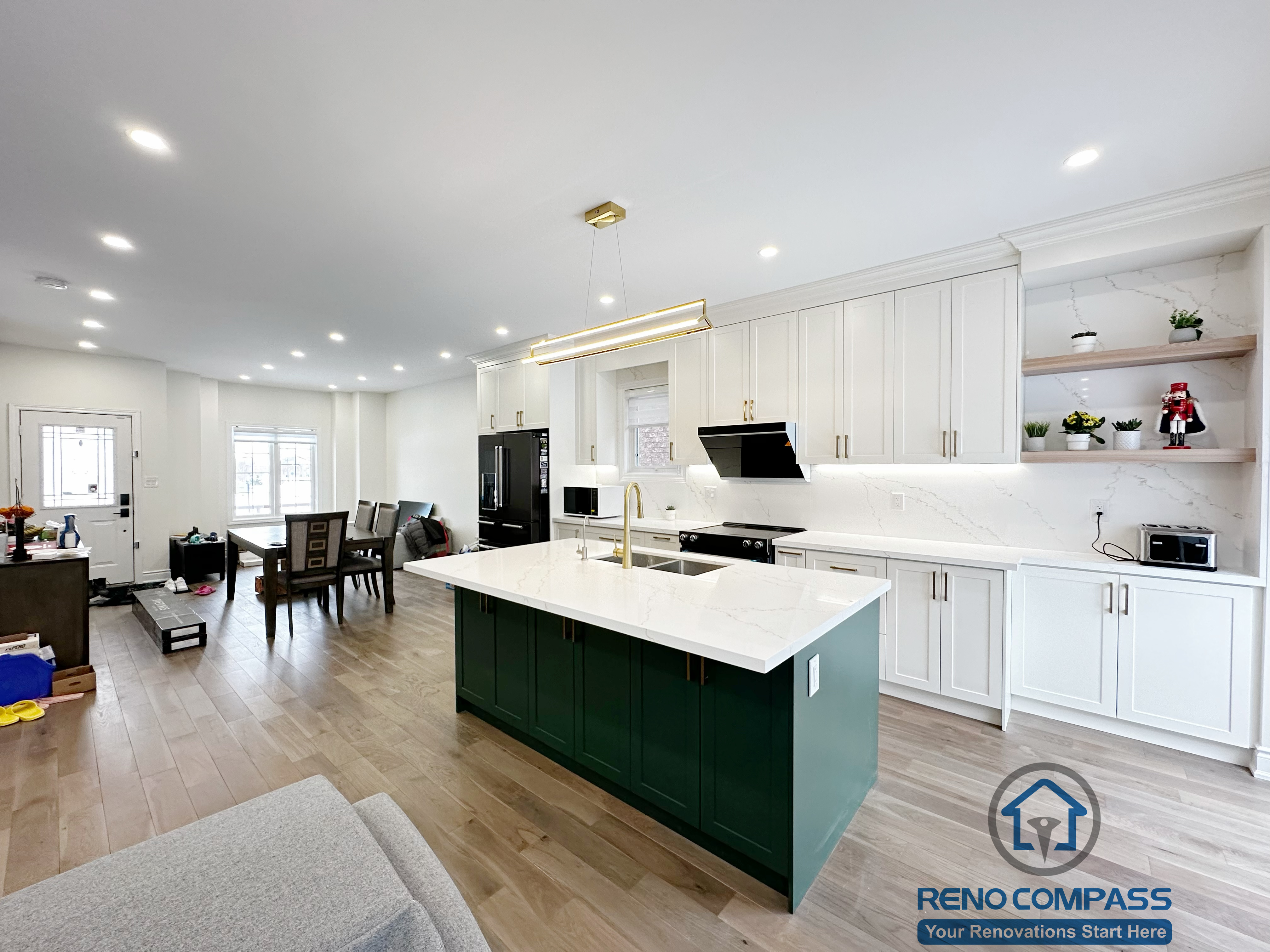 Interior renovation in Markham showcasing a modern kitchen with custom white cabinetry, a contrasting dark green island, quartz countertops, and integrated lighting. The open layout enhances functionality, flow, and everyday family use.
