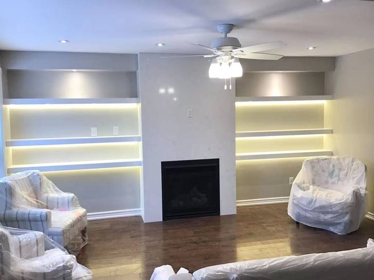 This Richmond Hill interior partial renovation highlights a modern living room upgrade featuring a custom fireplace feature wall with built-in illuminated shelving on both sides. Warm LED lighting enhances the display areas while creating a cozy and elegant ambiance. The renovated space includes upgraded flooring, recessed ceiling lights, and a clean contemporary layout designed for comfort and functionality. Completed by Reno Compass, this interior remodeling project adds both visual appeal and practical storage solutions, showcasing high-quality craftsmanship for homes across Richmond Hill and the Greater Toronto Area.