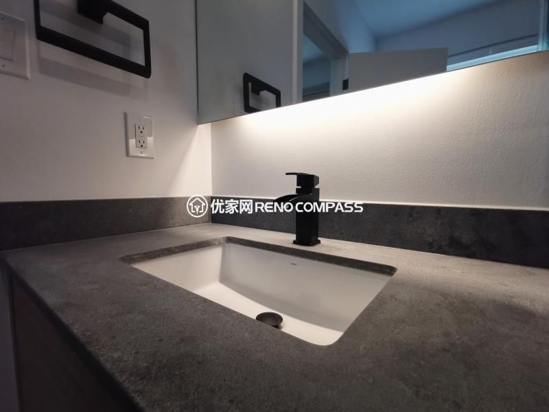 Bathroom sink detail from a North York interior renovation, featuring an integrated rectangular sink, stone countertop, and matte black faucet. The wall-mounted mirror with built-in LED lighting provides even illumination while maintaining a clean, minimalist appearance. Neutral material tones and concealed detailing enhance durability and ease of maintenance, reflecting a modern bathroom renovation completed by a Toronto renovation company focused on precision and functional design.