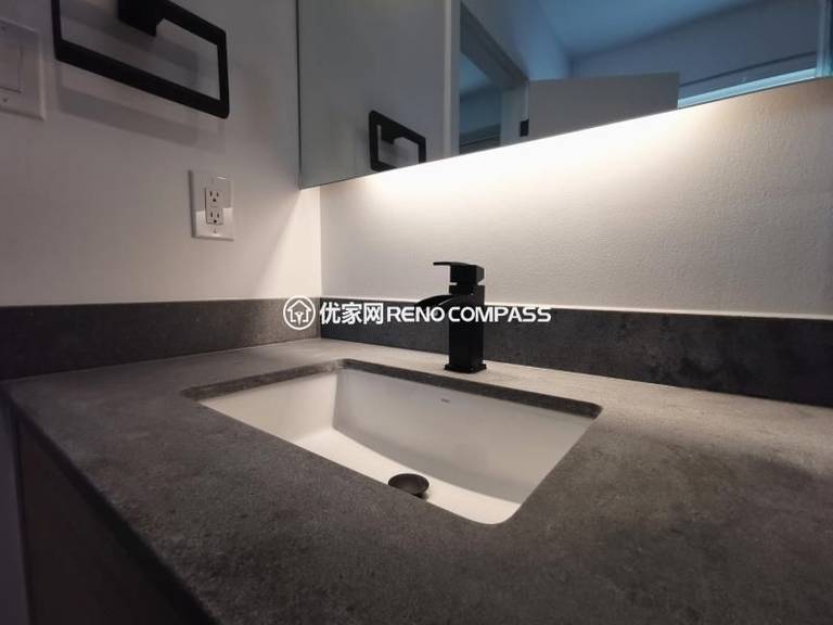 Bathroom sink detail from a North York interior renovation, featuring an integrated rectangular sink, stone countertop, and matte black faucet. The wall-mounted mirror with built-in LED lighting provides even illumination while maintaining a clean, minimalist appearance. Neutral material tones and concealed detailing enhance durability and ease of maintenance, reflecting a modern bathroom renovation completed by a Toronto renovation company focused on precision and functional design.