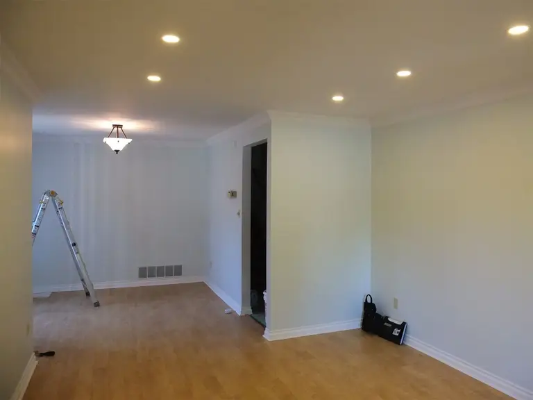 This Oshawa interior renovation highlights a fully refreshed living room with upgraded recessed pot lights, smooth ceiling finish, and newly refinished hardwood flooring. The large front-facing window enhances natural daylight, creating a bright and welcoming atmosphere. Neutral wall tones combined with detailed crown molding provide a clean and modern aesthetic. The optimized lighting layout improves both functionality and visual depth of the space. Completed by a professional Toronto Renovation Company, this project demonstrates quality craftsmanship and thoughtful interior enhancement.