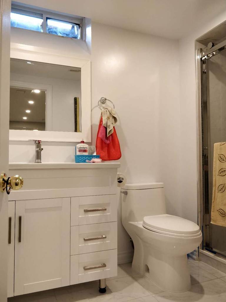 This image showcases the newly renovated basement bathroom in Scarborough, featuring a modern white vanity with integrated storage drawers, a sleek undermount sink, and a framed mirror for a clean and functional design. The space also includes a contemporary toilet and a glass-enclosed shower, maximizing comfort and usability within a compact layout. Light-colored tile flooring enhances brightness and creates a fresh, contemporary atmosphere. Completed by Reno Compass Inc., this basement bathroom renovation combines practical space planning with modern finishes for everyday convenience.