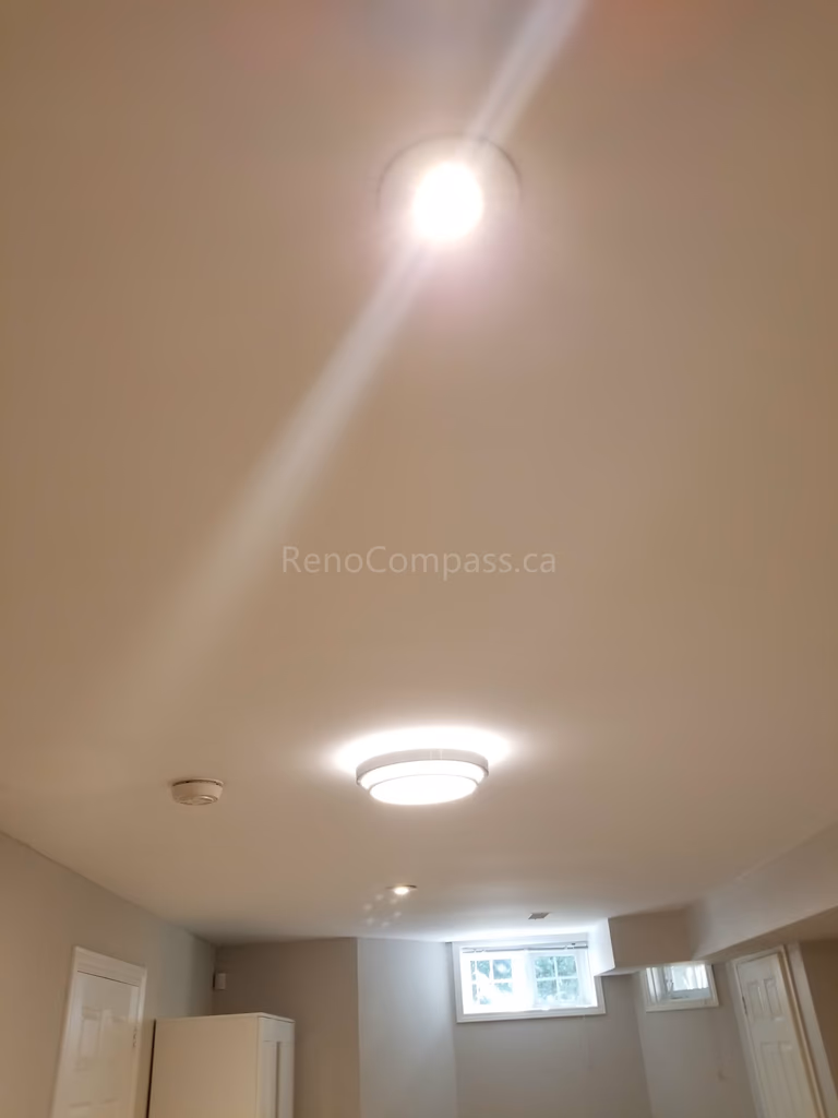 This Toronto basement renovation features newly installed ceiling lighting, including modern pot lights and flush mount fixtures to brighten the entire space. The upgraded lighting design improves visibility, enhances ambiance, and creates a clean, modern basement living environment. Completed by Reno Compass Inc., this lighting installation adds both functionality and contemporary style to the finished basement.