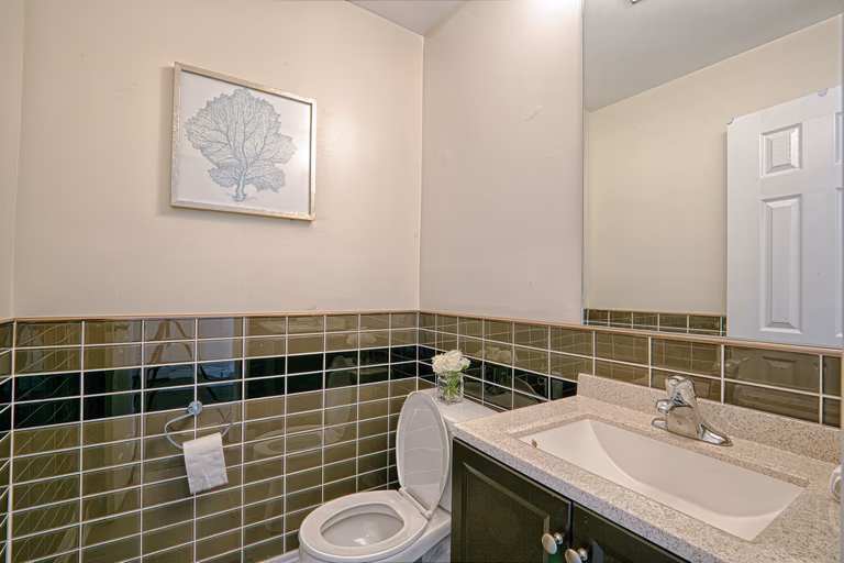 This modern bathroom renovation features a clean vanity design with a durable quartz countertop, contemporary sink, and large mirror to enhance brightness and space perception. The decorative horizontal tile detailing adds texture and visual interest while maintaining a sleek and neutral palette. Designed for both practicality and style, this bathroom upgrade reflects the craftsmanship of a professional Toronto renovation company delivering refined interior renovation solutions for modern homes.
