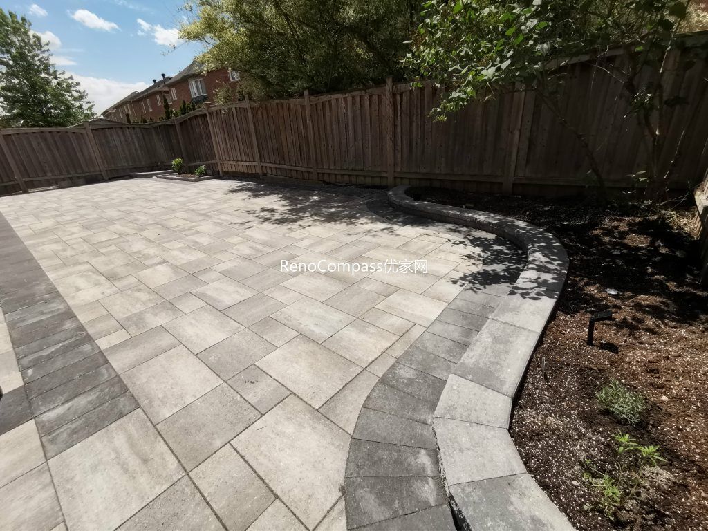 Backyard interlocking patio project in Richmond Hill designed around a wooden deck. Featuring clean, neutral-toned stones arranged for durability and aesthetic appeal — a perfect balance of function and style by Reno Compass.