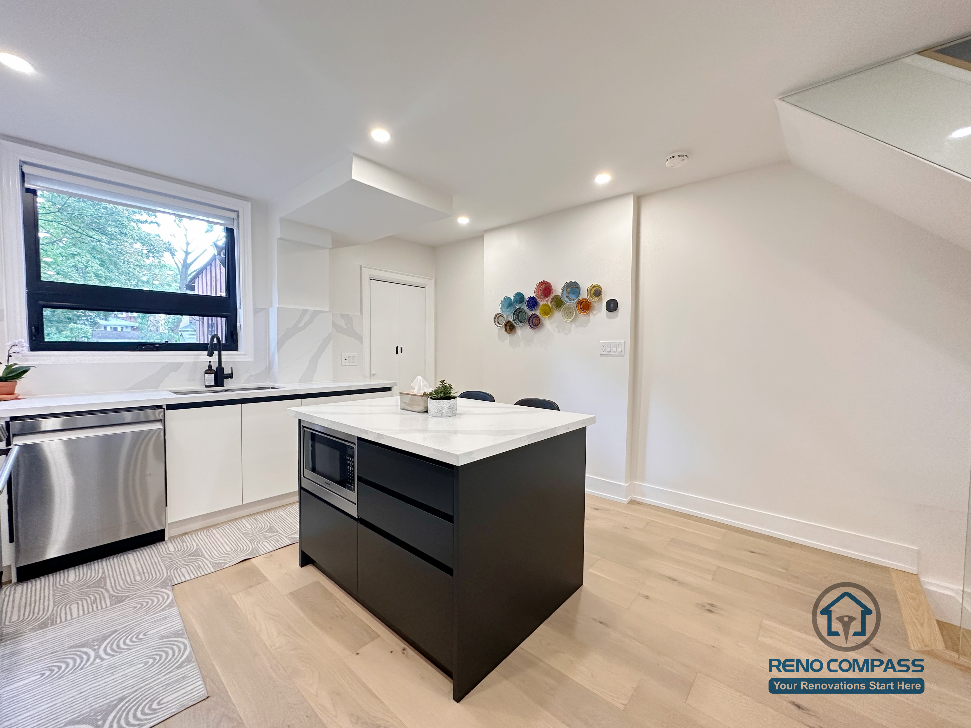 This Toronto interior renovation showcases a modern white kitchen featuring flat-panel cabinetry, a quartz waterfall island, stainless steel appliances, and recessed ceiling lighting. The clean lines and functional layout highlight contemporary kitchen design and quality workmanship delivered by a professional Toronto renovation company.