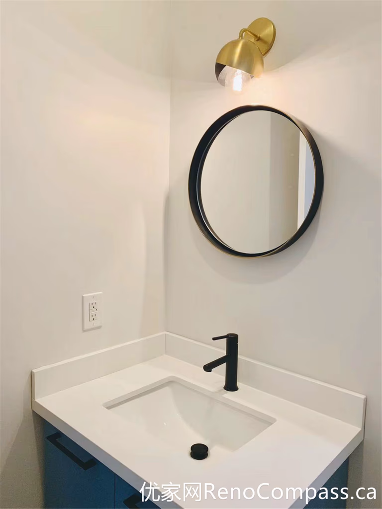 This Markham bathroom renovation features a compact vanity setup enhanced by a round mirror and a warm-toned wall sconce. The combination of soft lighting, matte black faucet, and clean white surfaces creates a cozy yet modern atmosphere, ideal for smaller bathroom spaces.