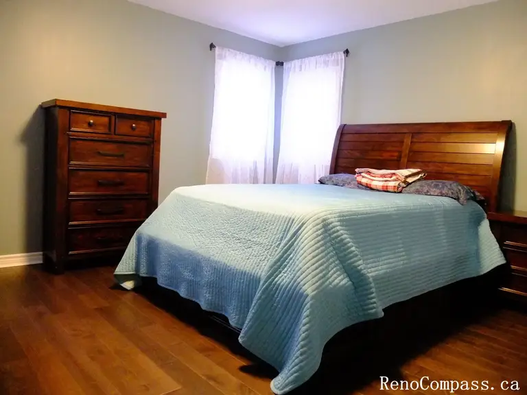 This Richmond Hill interior renovation showcases a bright and practical bedroom featuring hardwood flooring, natural light from large windows, and a functional furniture layout. The space includes a workspace area and storage solutions, creating a comfortable and well-organized environment. Completed by a Toronto renovation company, this design emphasizes simplicity, usability, and modern living.