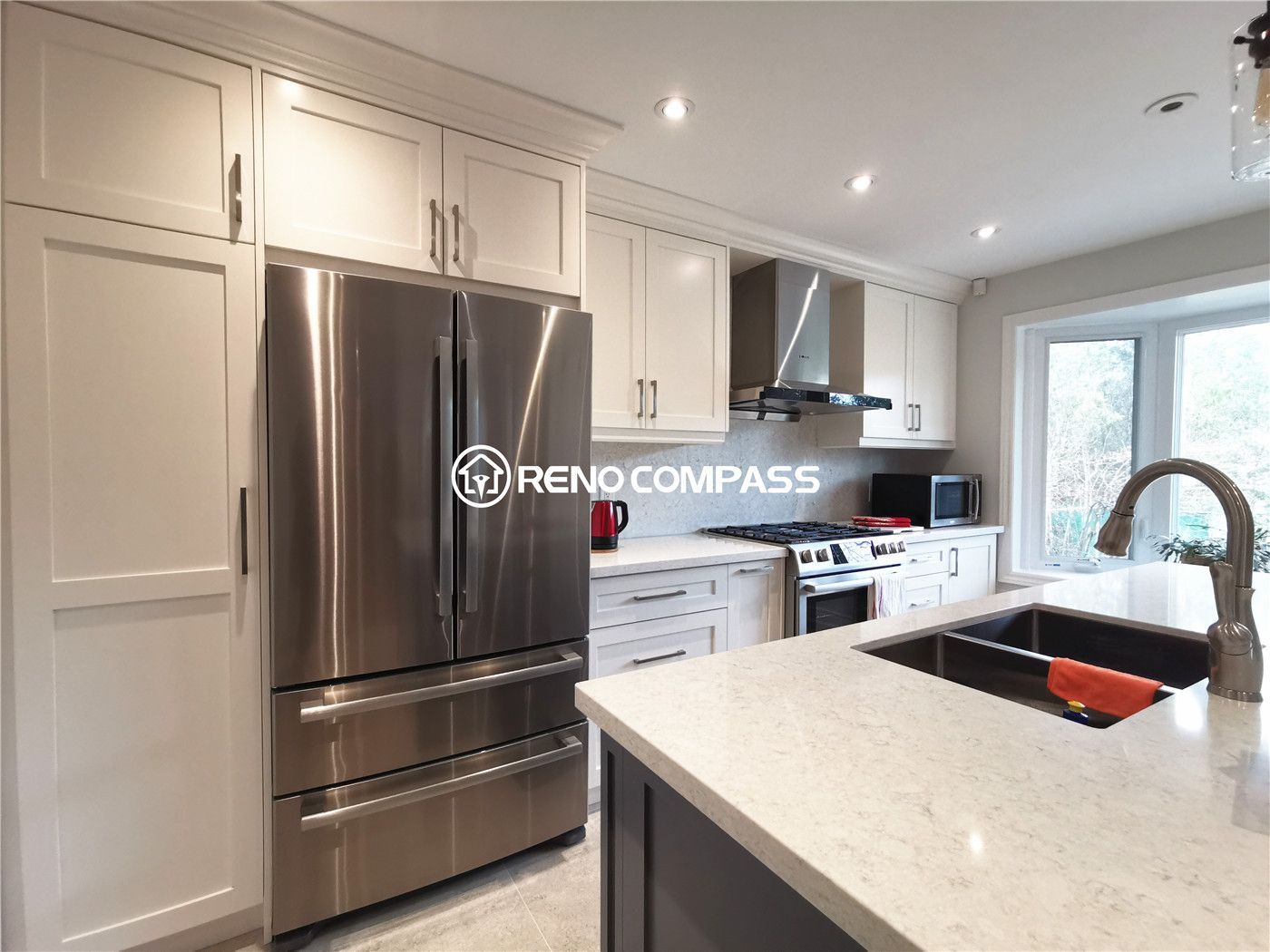 This kitchen appliance wall is part of a North York interior renovation, showcasing custom cabinetry designed for both storage and visual continuity. Full-height shaker-style cabinets frame the stainless steel refrigerator, while quartz countertops and a clean backsplash create a cohesive and durable work surface. Recessed ceiling lights provide even illumination, and the efficient layout supports everyday cooking and organization. The refined material selection and functional planning reflect the standards expected from a professional Toronto interior renovation project.