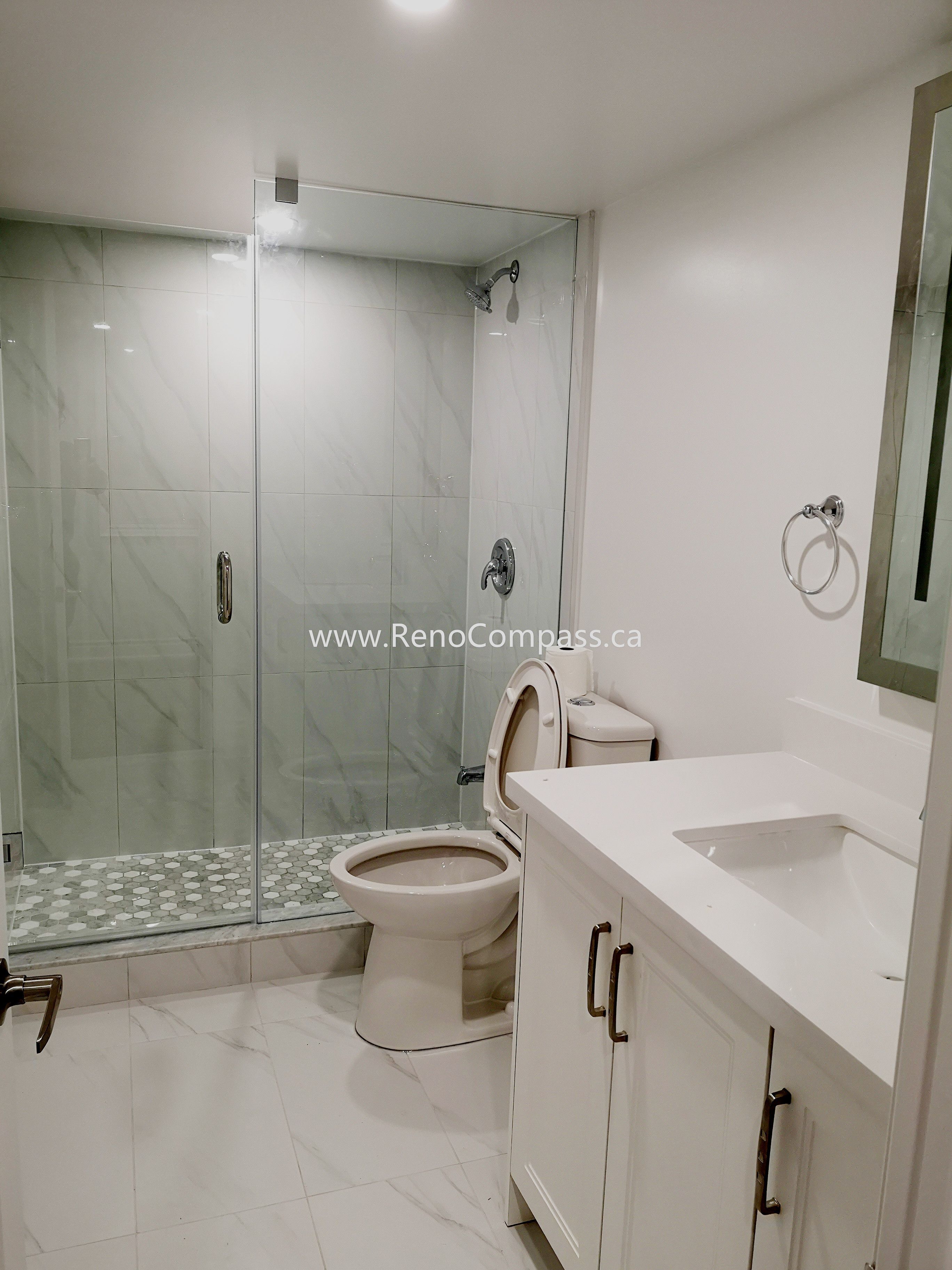 This Vaughan basement bathroom renovation showcases a modern glass shower enclosure with elegant marble-style wall tiles and a clean, minimalist layout. The upgraded space includes a sleek vanity, contemporary fixtures, and durable floor tiles designed for both style and functionality. Completed by Reno Compass Inc., this basement bathroom upgrade enhances comfort, increases home value, and creates a bright, modern space that complements the fully renovated basement.