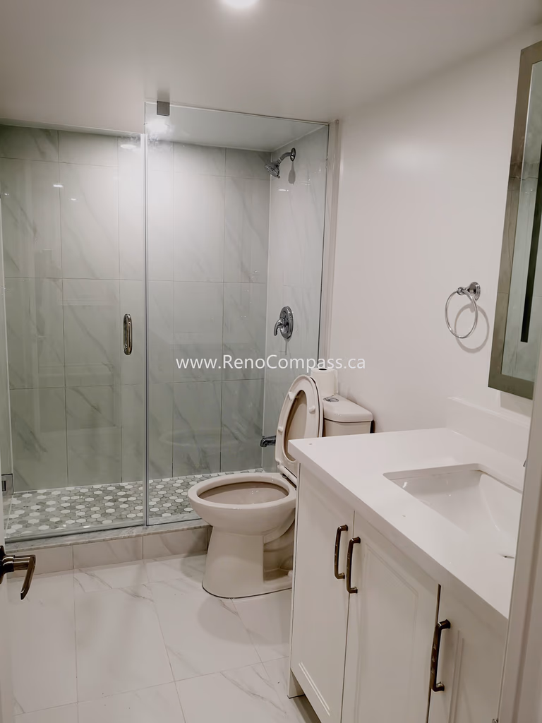 This Vaughan basement bathroom renovation showcases a modern glass shower enclosure with elegant marble-style wall tiles and a clean, minimalist layout. The upgraded space includes a sleek vanity, contemporary fixtures, and durable floor tiles designed for both style and functionality. Completed by Reno Compass Inc., this basement bathroom upgrade enhances comfort, increases home value, and creates a bright, modern space that complements the fully renovated basement.