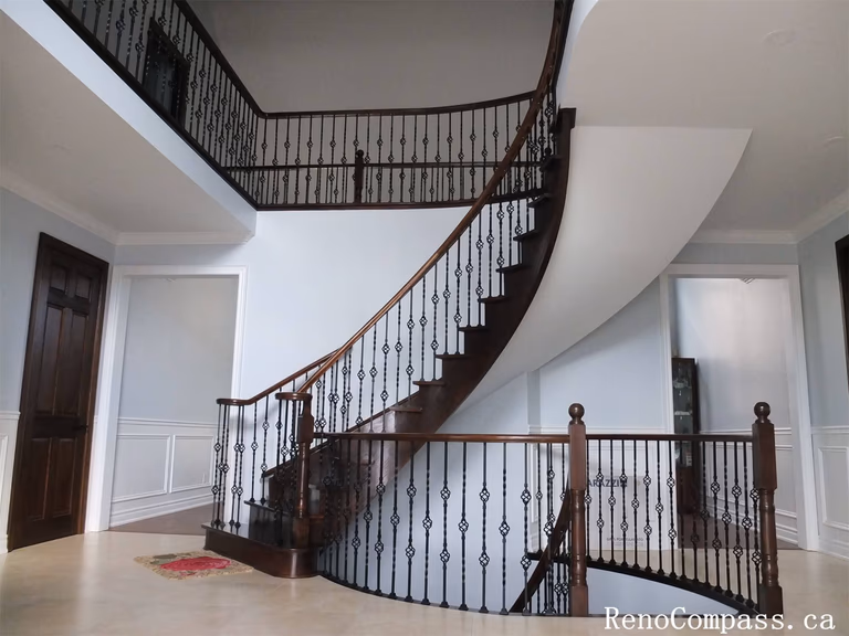 This Richmond Hill interior renovation features an elegant curved staircase with dark wood steps and custom wrought iron railings. The staircase repainting and refinishing enhance the home's architectural beauty while creating a refined transition between floors.
