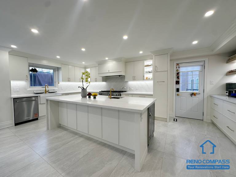 This kitchen renovation features a bright, open layout centered around a large island that enhances both functionality and flow. Custom white cabinetry, quartz countertops, and integrated appliances create a clean, cohesive look, while recessed ceiling lighting ensures even illumination throughout the space. The design balances everyday usability with a timeless, modern aesthetic.