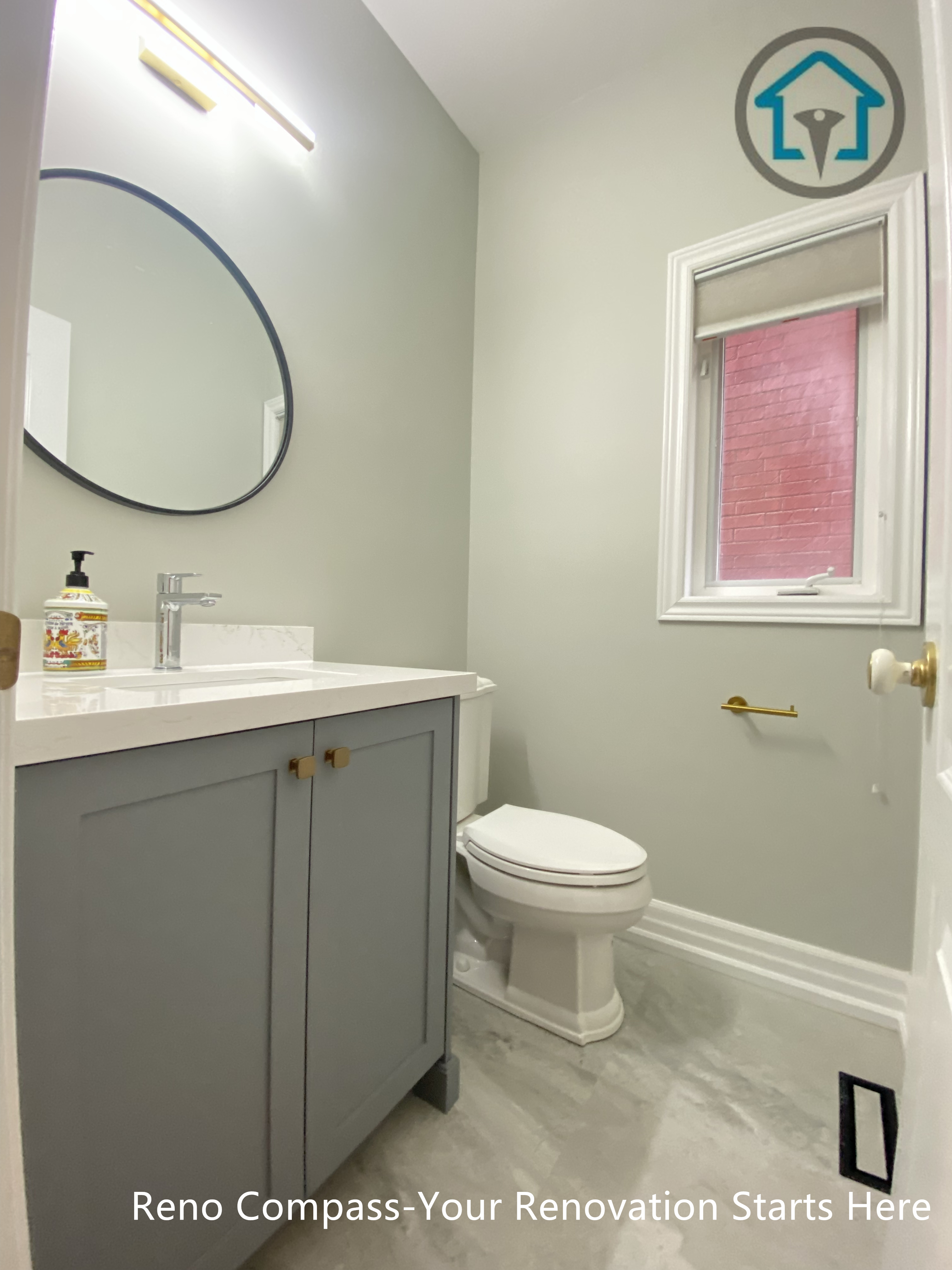 This vanity area combines soft grey cabinetry with clean-lined hardware and a round mirror to create a balanced, modern look. A quartz countertop enhances durability and ease of maintenance, while the compact layout ensures efficient use of space. Natural light from the window keeps the bathroom bright and comfortable for daily use.