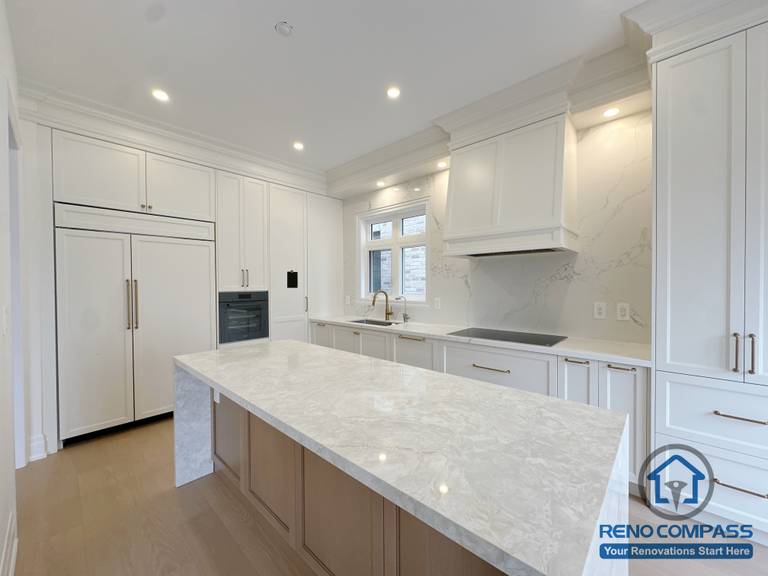 Modern kitchen renovation in Toronto featuring a large waterfall island, built-in refrigerator, and custom cabinetry, designed for functionality and clean aesthetics.