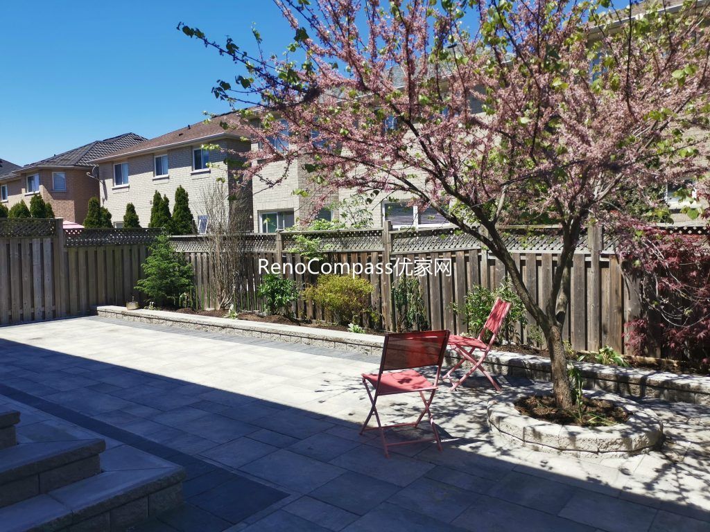 Modern Mississauga backyard patio featuring interlocking stone flooring, raised retaining wall, and landscaped garden beds, creating a functional and elegant outdoor living space.
