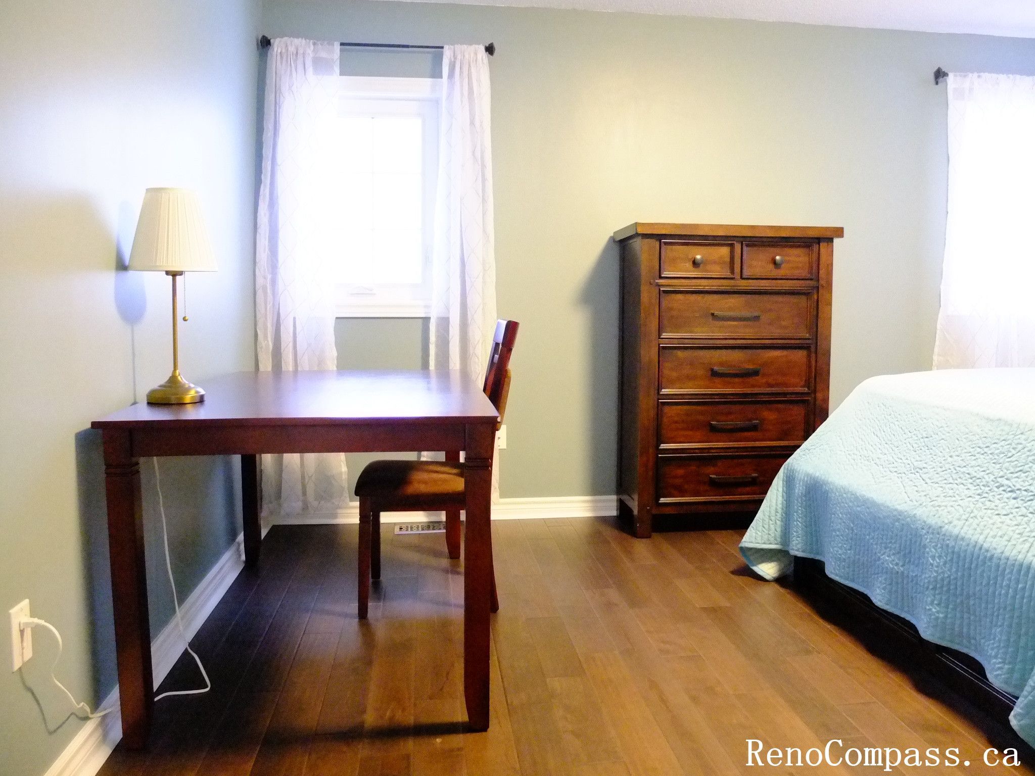 This Richmond Hill interior renovation showcases a bright and practical bedroom featuring hardwood flooring, natural light from large windows, and a functional furniture layout. The space includes a workspace area and storage solutions, creating a comfortable and well-organized environment. Completed by a Toronto renovation company, this design emphasizes simplicity, usability, and modern living.