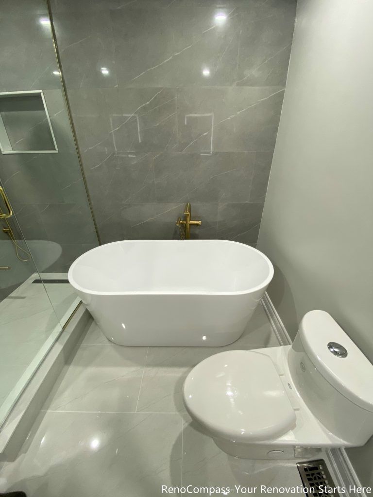 This Oakville master bathroom renovation features a sleek freestanding bathtub paired with premium gold floor-mounted fixtures and large-format marble-look wall tiles. The clean layout integrates a glass-enclosed shower and modern toilet placement, creating a functional yet luxurious spa-style bathroom environment. Completed by a professional Toronto renovation company, this upgrade enhances comfort, improves space efficiency, and delivers a timeless modern design that increases both daily living quality and overall property value.