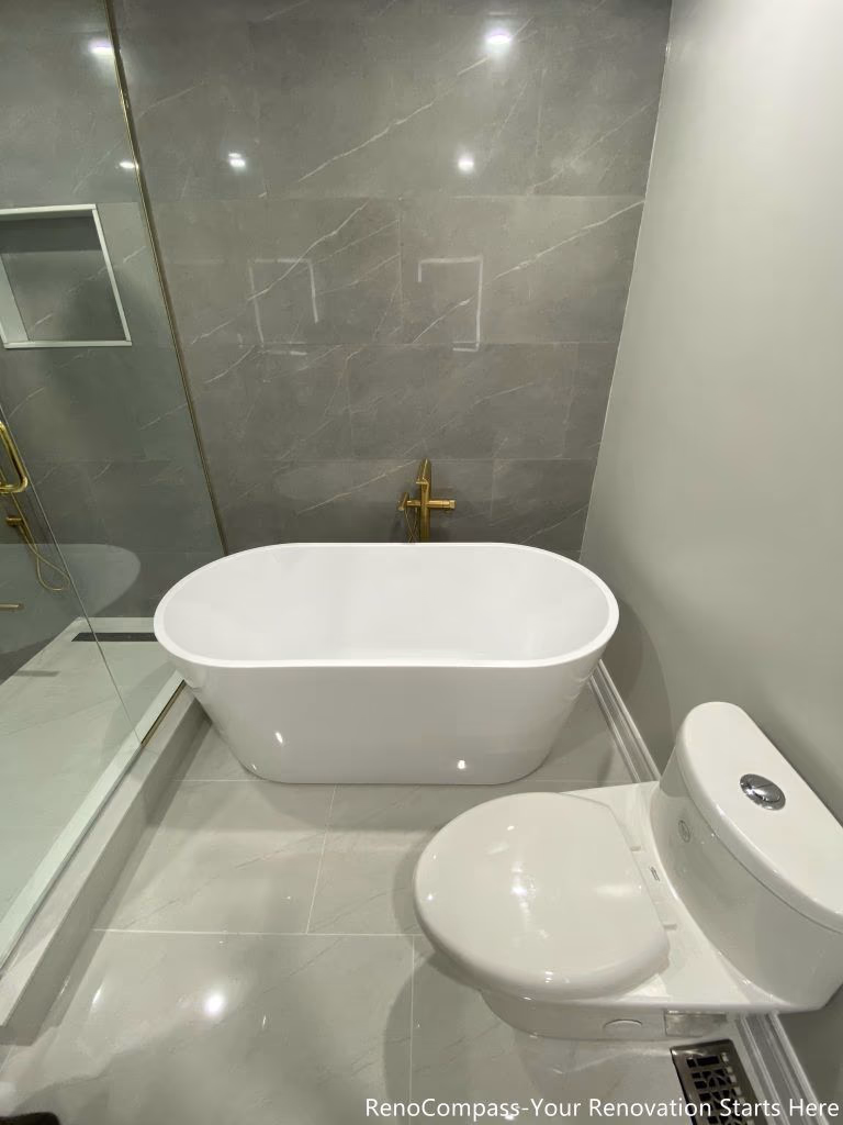 This Oakville master bathroom renovation features a sleek freestanding bathtub paired with premium gold floor-mounted fixtures and large-format marble-look wall tiles. The clean layout integrates a glass-enclosed shower and modern toilet placement, creating a functional yet luxurious spa-style bathroom environment. Completed by a professional Toronto renovation company, this upgrade enhances comfort, improves space efficiency, and delivers a timeless modern design that increases both daily living quality and overall property value.