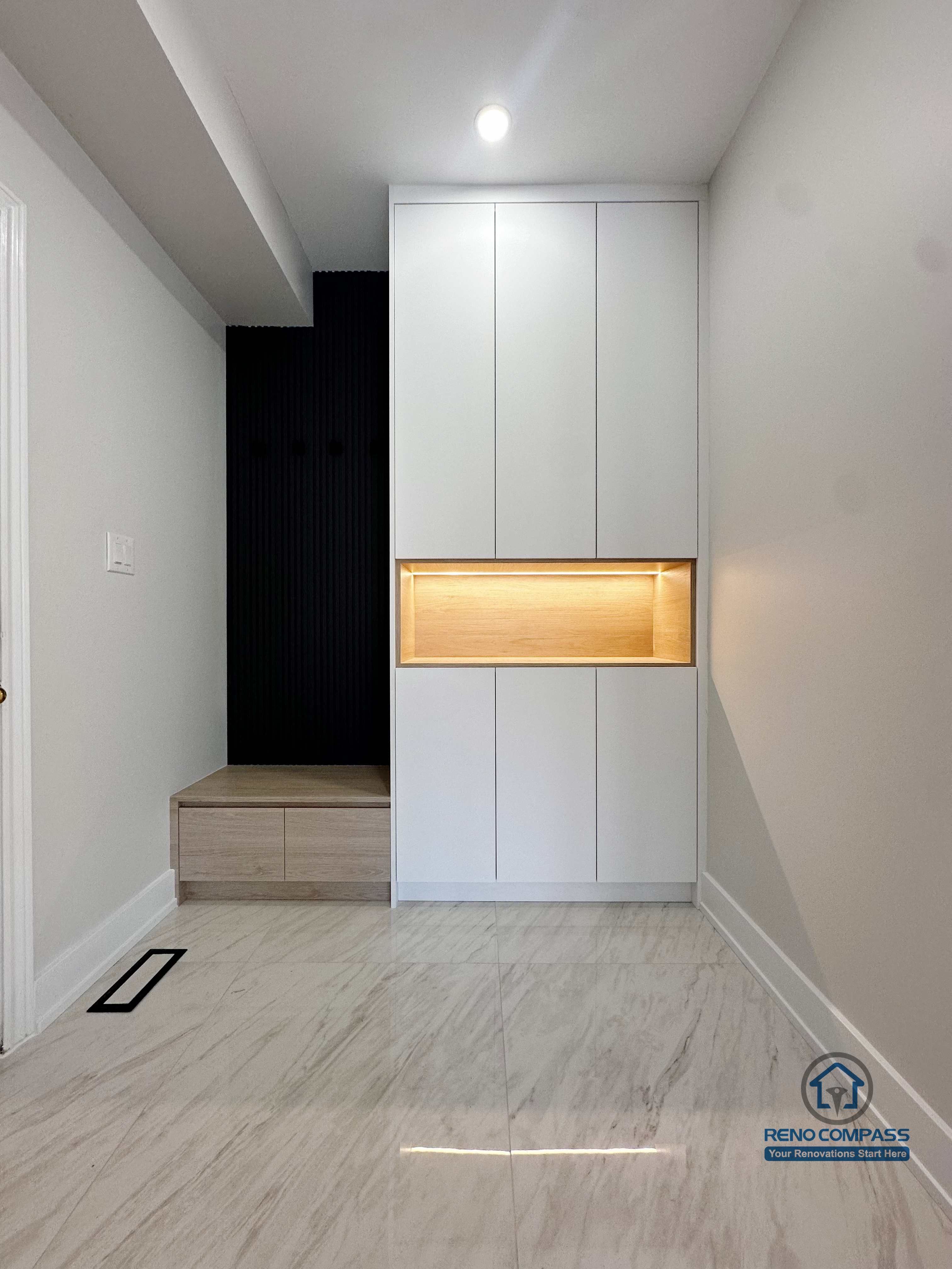 This Markham interior renovation features a custom-built entryway storage system designed to improve daily functionality while maintaining a clean, modern aesthetic. Full-height cabinetry provides concealed storage, while the integrated wood-accent niche with warm backlighting adds visual focus and practical surface space. The recessed bench area creates a convenient transition zone for shoes and outerwear, making the entry both organized and welcoming. Neutral finishes and integrated lighting ensure the space feels bright, efficient, and well-balanced.