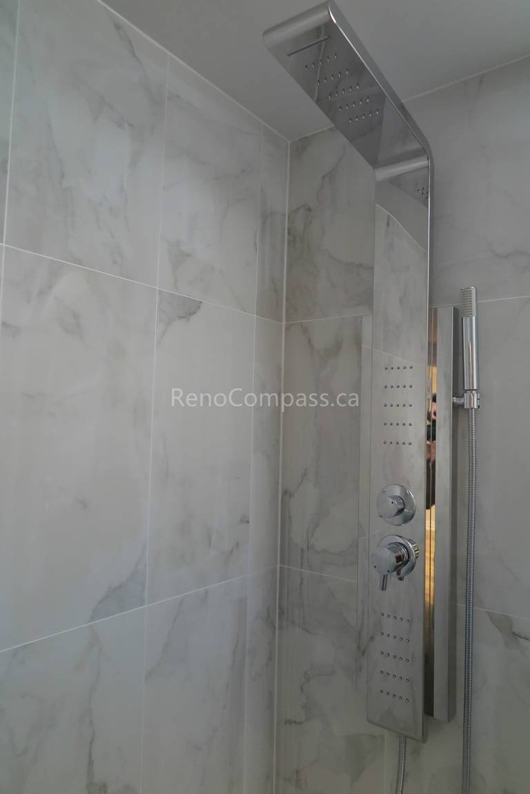 Close-up of a modern rain shower system installed during a North York interior renovation. The image features large-format marble-look wall tiles, a multi-function shower panel, and precise waterproof detailing, completed by a professional Toronto renovation company focused on durability, comfort, and high-end bathroom finishes.