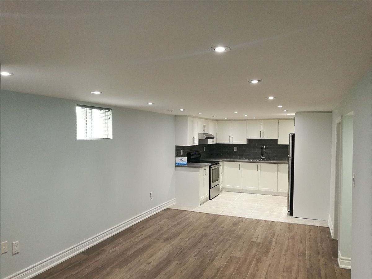 Open-concept basement interior renovation in Pickering featuring continuous wood-look flooring, recessed pot lighting, and a modern white kitchen with dark tile backsplash. This bright and functional layout maximizes usable living space and demonstrates the quality craftsmanship of a professional Toronto renovation company.