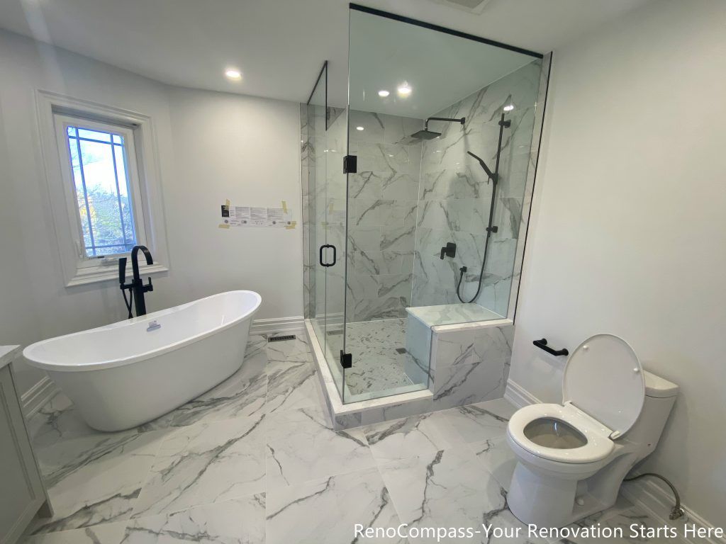 This Thornhill master bathroom renovation showcases a spacious and modern layout featuring a freestanding bathtub, a walk-in glass shower, and large-format marble-look porcelain tiles. The frameless glass shower enclosure enhances visual openness, while matte black fixtures provide a refined contrast against the light stone surfaces. The combination of a built-in shower bench, patterned shower base, and bright natural light creates a functional, elegant, and comfortable bathroom designed for long-term daily use.