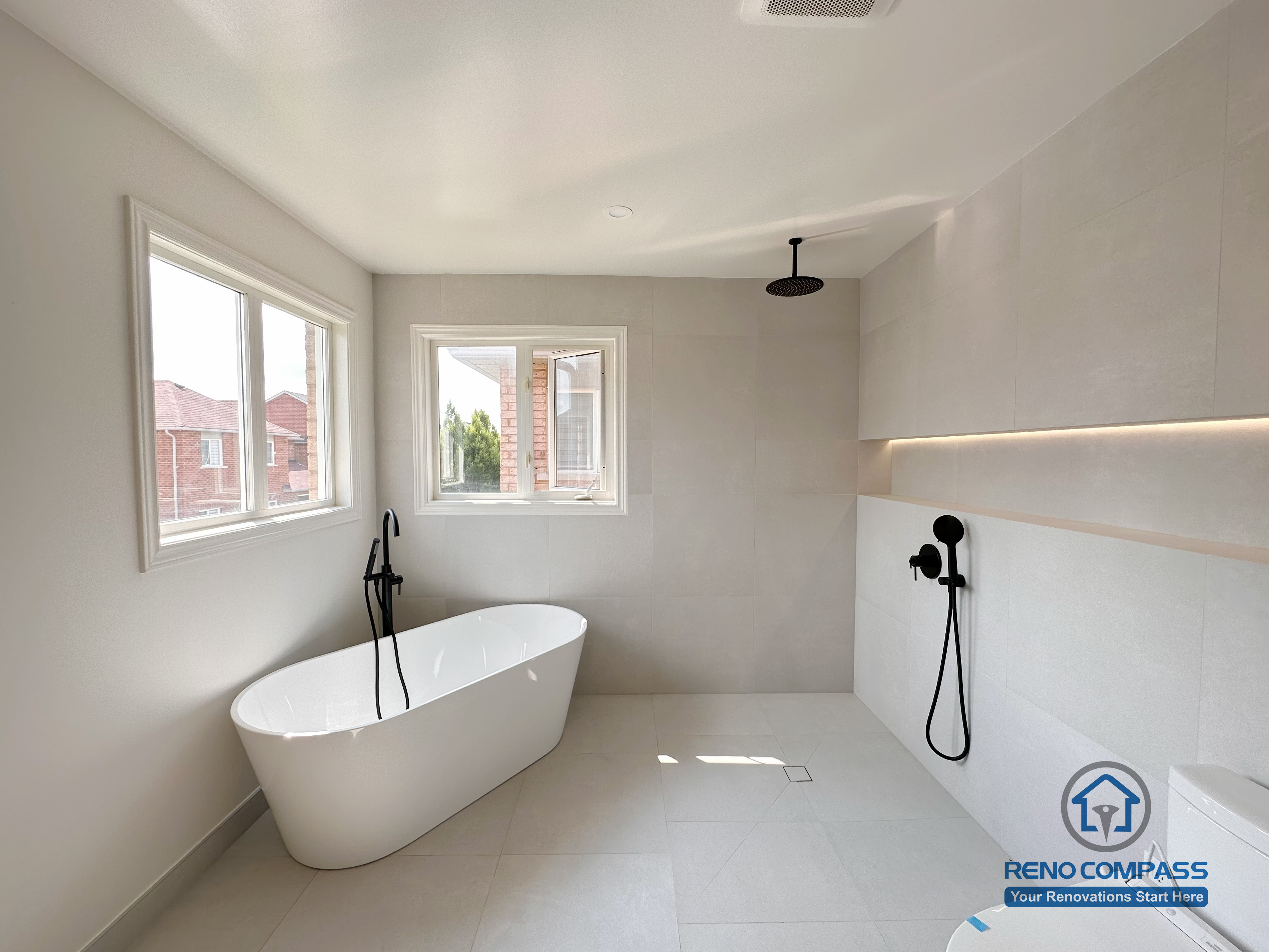 Modern bathroom renovation in Markham featuring a freestanding bathtub, walk-in shower, and wall-mounted matte black fixtures. Large-format tiles, soft natural light, and a minimalist layout create a calm, spa-like bathroom designed for comfort and everyday use.